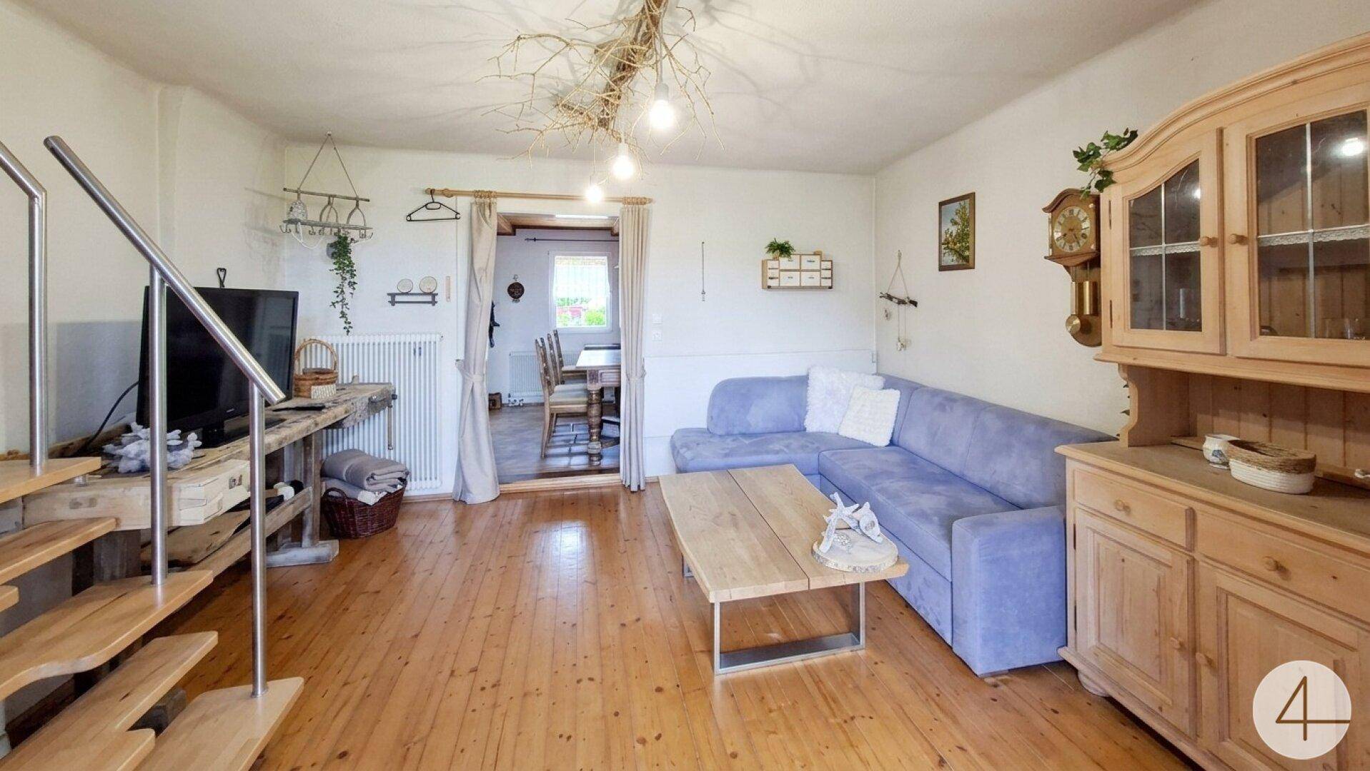 Helles Wohnzimmer mit Ecksofa, Holzboden und offener Holztreppe.