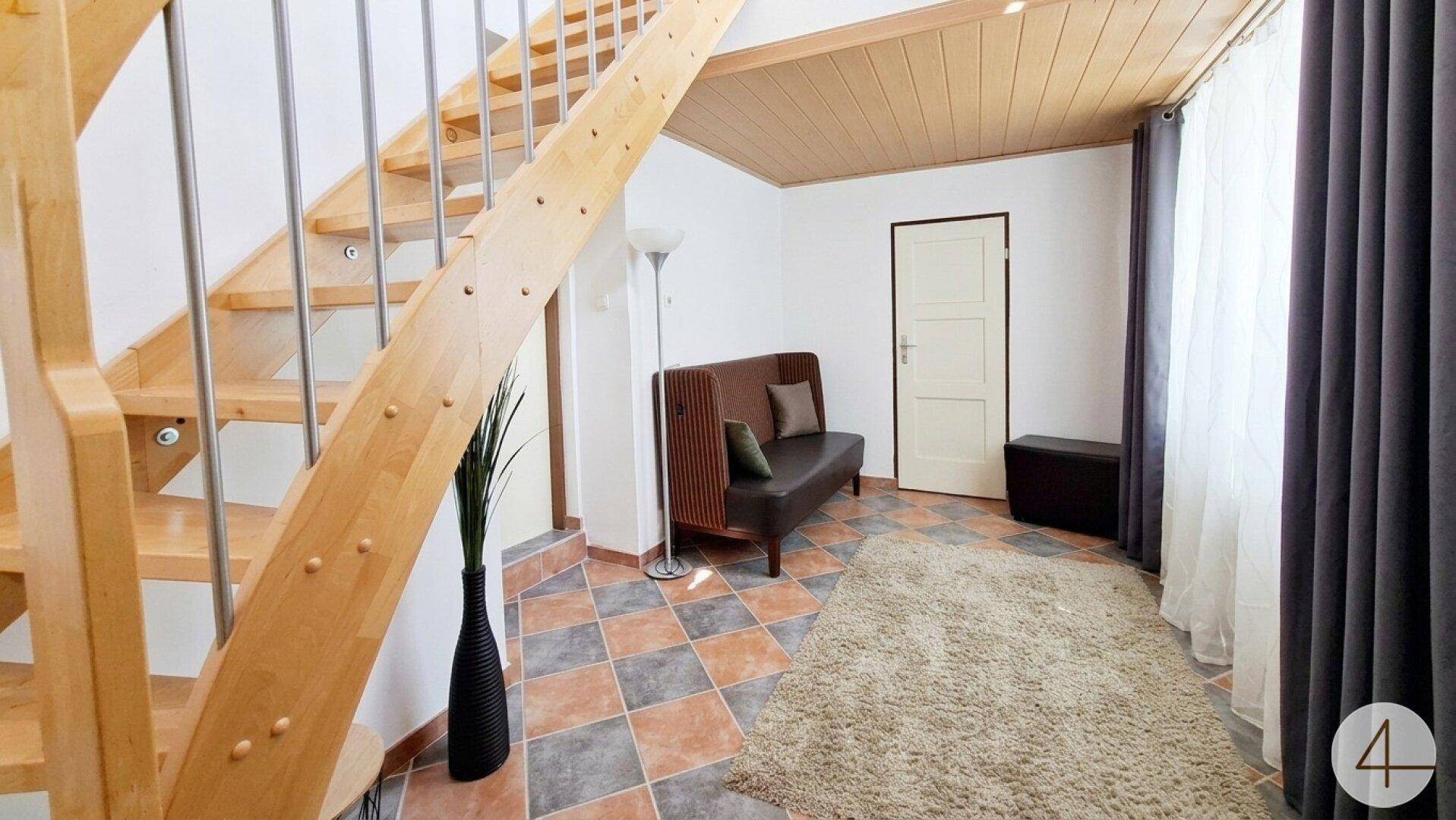 Eingangsbereich mit offener Holztreppe, gemusterten Fliesen und Holzdecke.