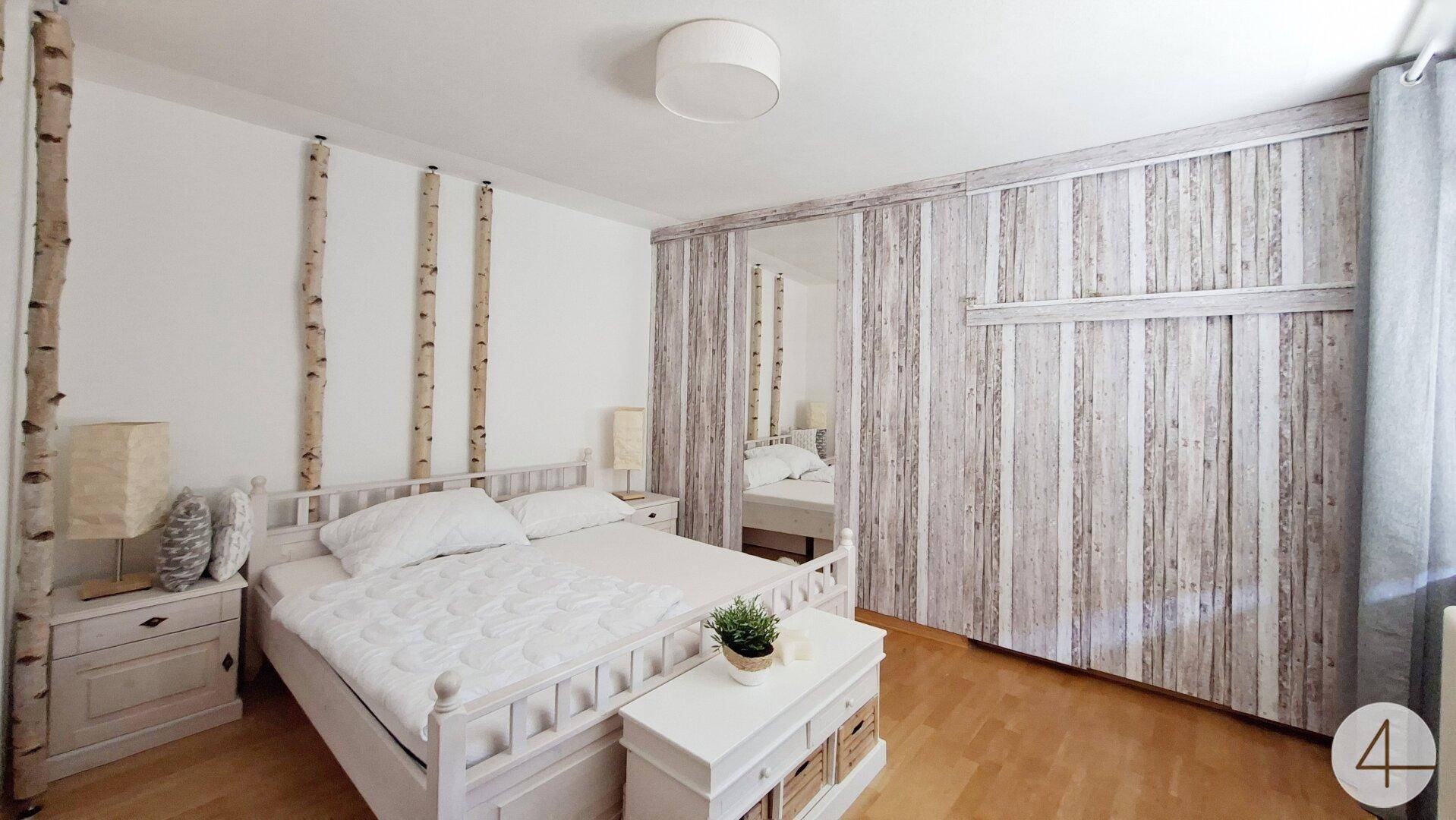 Schlafzimmer mit weißem Bett, dekorativen Holzelementen und Schiebetüren im Holzdesign.