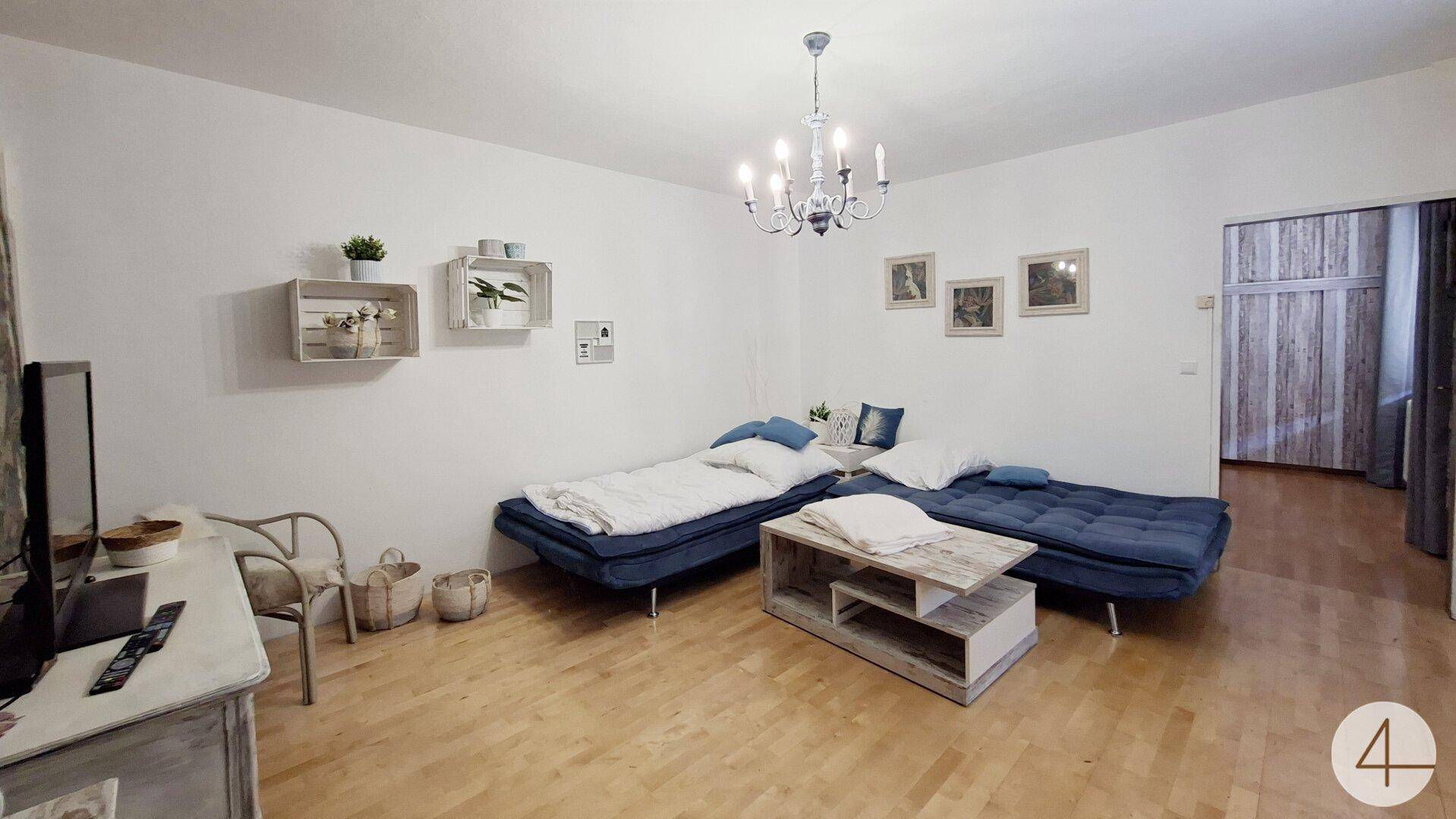 Wohnzimmer mit zwei blauen Schlafsofas, Holztisch und Parkettboden.
