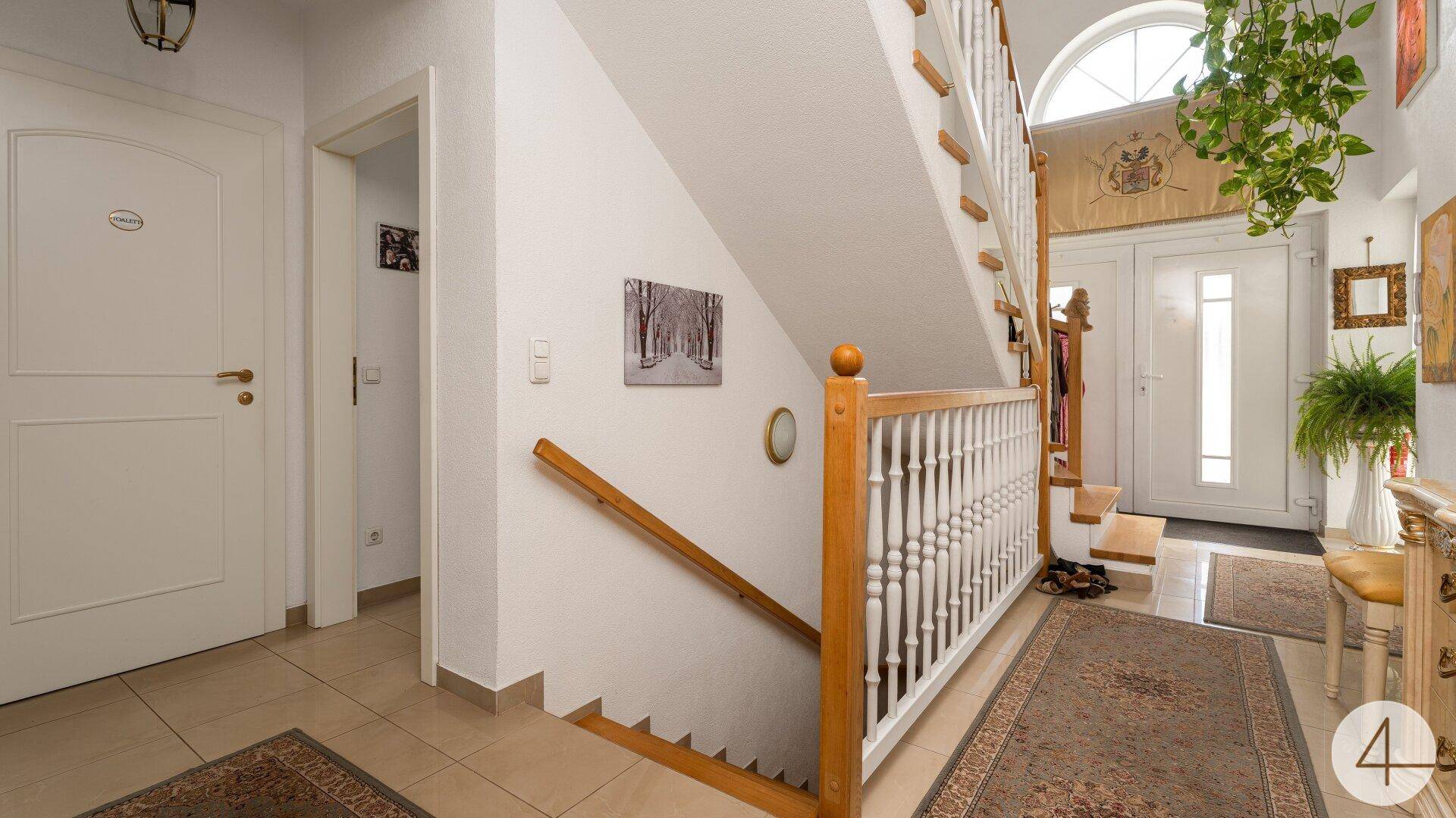 Geräumiger Eingangsbereich mit Holztreppe, Fliesenboden und viel natürlichem Licht.