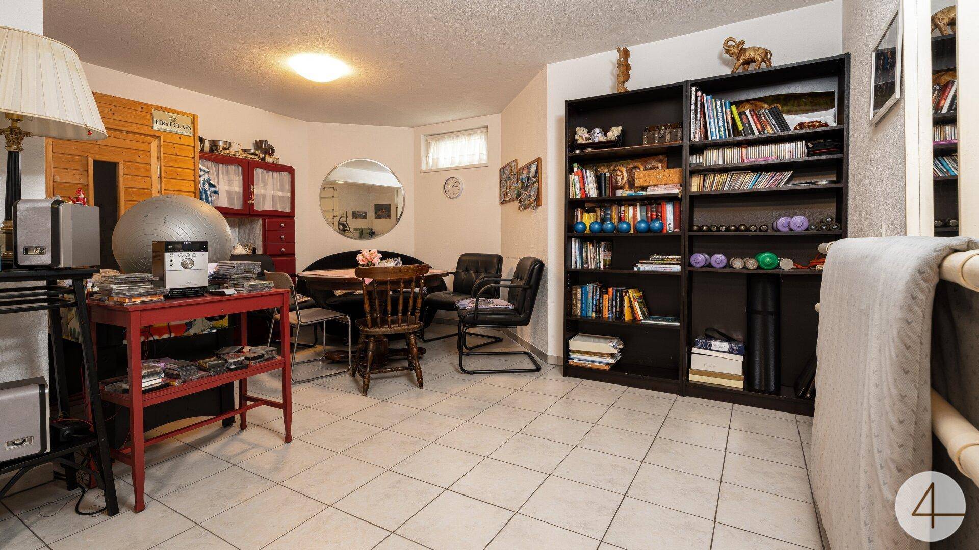 Gemütlicher Kellerraum mit Bücherregalen, Esstisch und Fliesenboden, ideal als Hobbyraum.