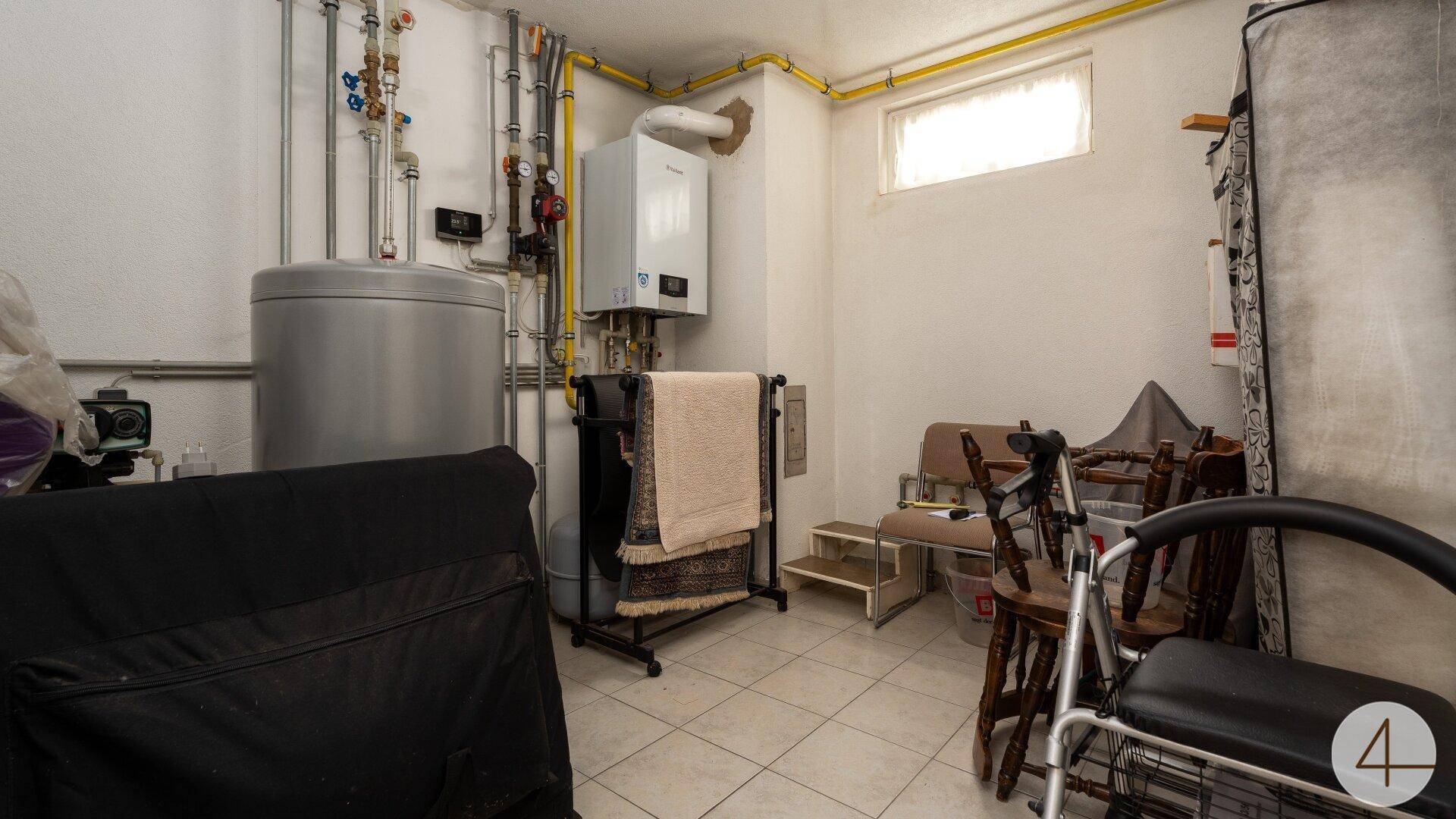 Heizungsraum im Keller mit Warmwasserspeicher, Heizkessel und sichtbaren Rohrleitungen.