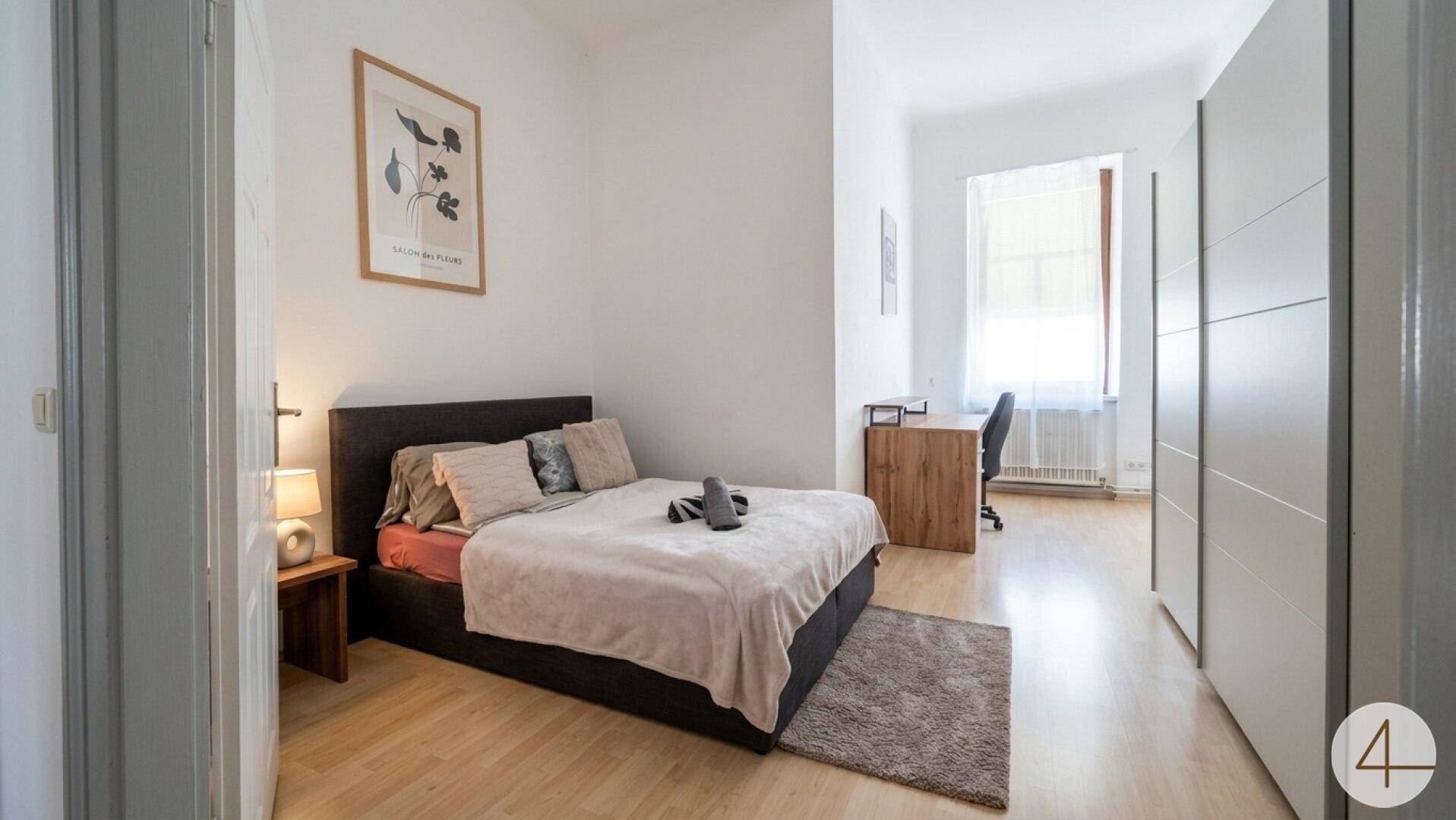 Schlafzimmer mit Doppelbett, Kleiderschrank und Schreibtischbereich.