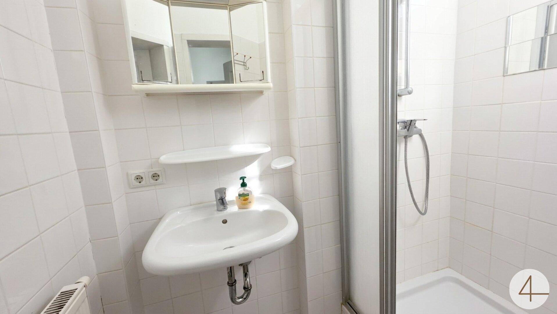 Kleines Badezimmer mit Dusche, Waschbecken und weißen Fliesen.