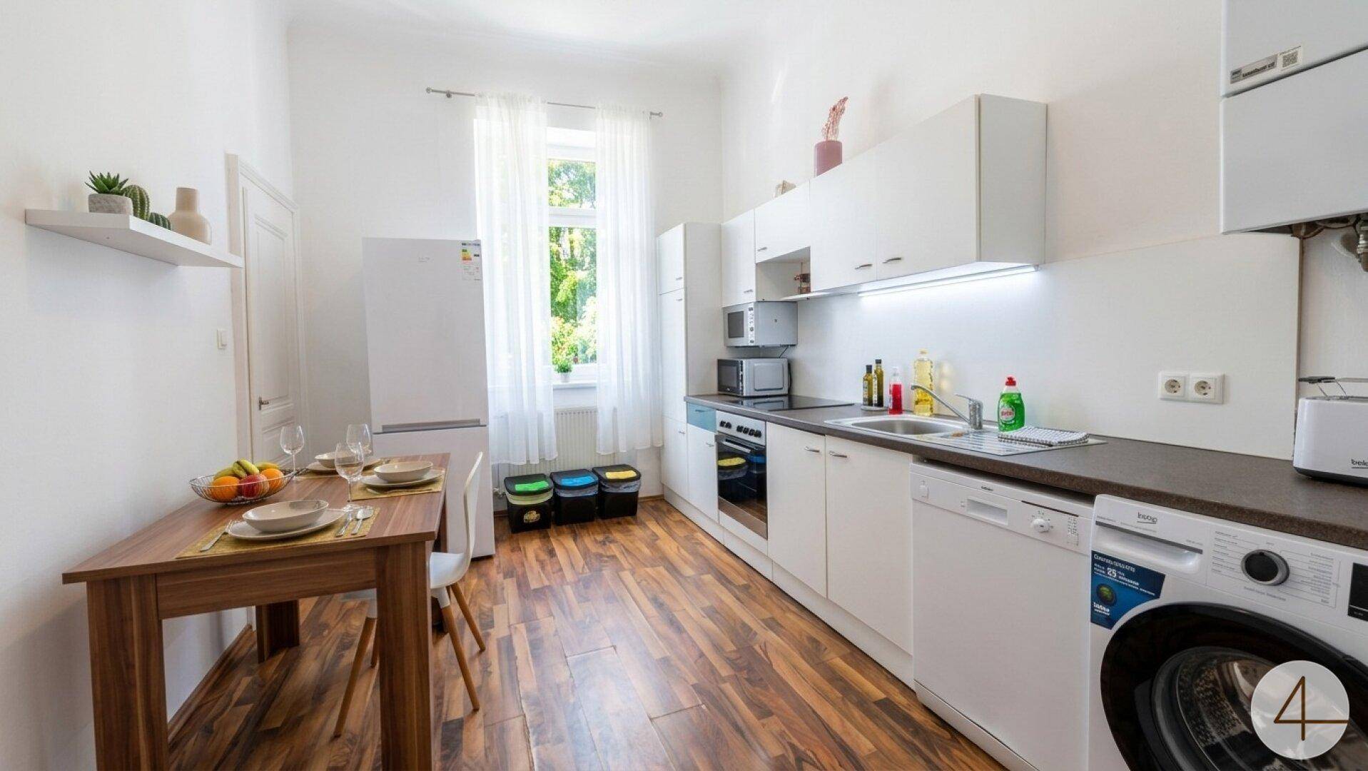 Funktionale Küche mit Essbereich, weißen Schränken und Waschmaschine.