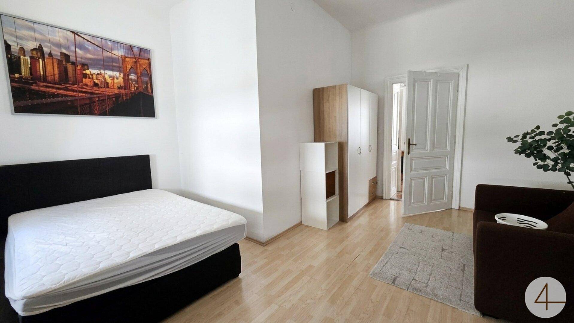Schlafzimmer mit Bett, Sofa und Kleiderschrank in hellem Ambiente.