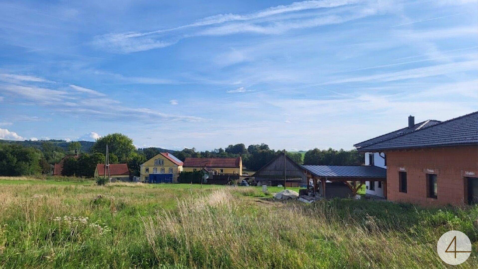 Weitläufiges unbebautes Grundstück mit Blick auf umliegende Häuser und ländliche Umgebung.