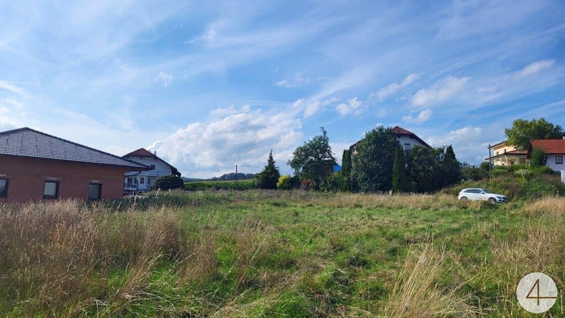 Grünes Baugrundstück mit umliegenden Wohnhäusern und einem geparkten Fahrzeug am Hang.