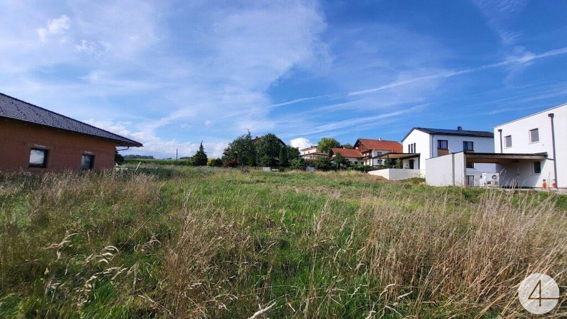 Unbebautes Grundstück mit Blick auf moderne Wohnhäuser und offene Landschaft.