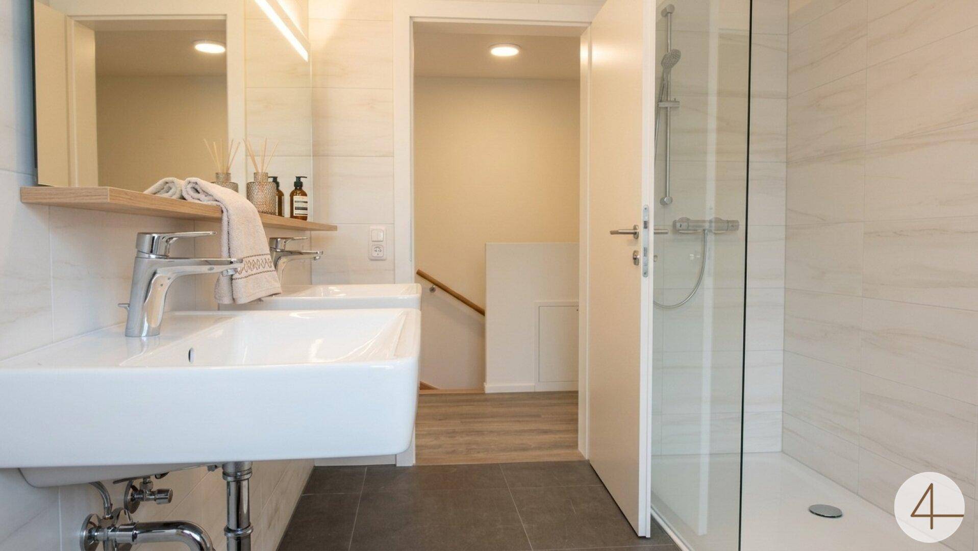 Modernes Badezimmer mit Doppelwaschbecken, großer Spiegelfläche und begehbarer Dusche in hellen Farbtönen.
