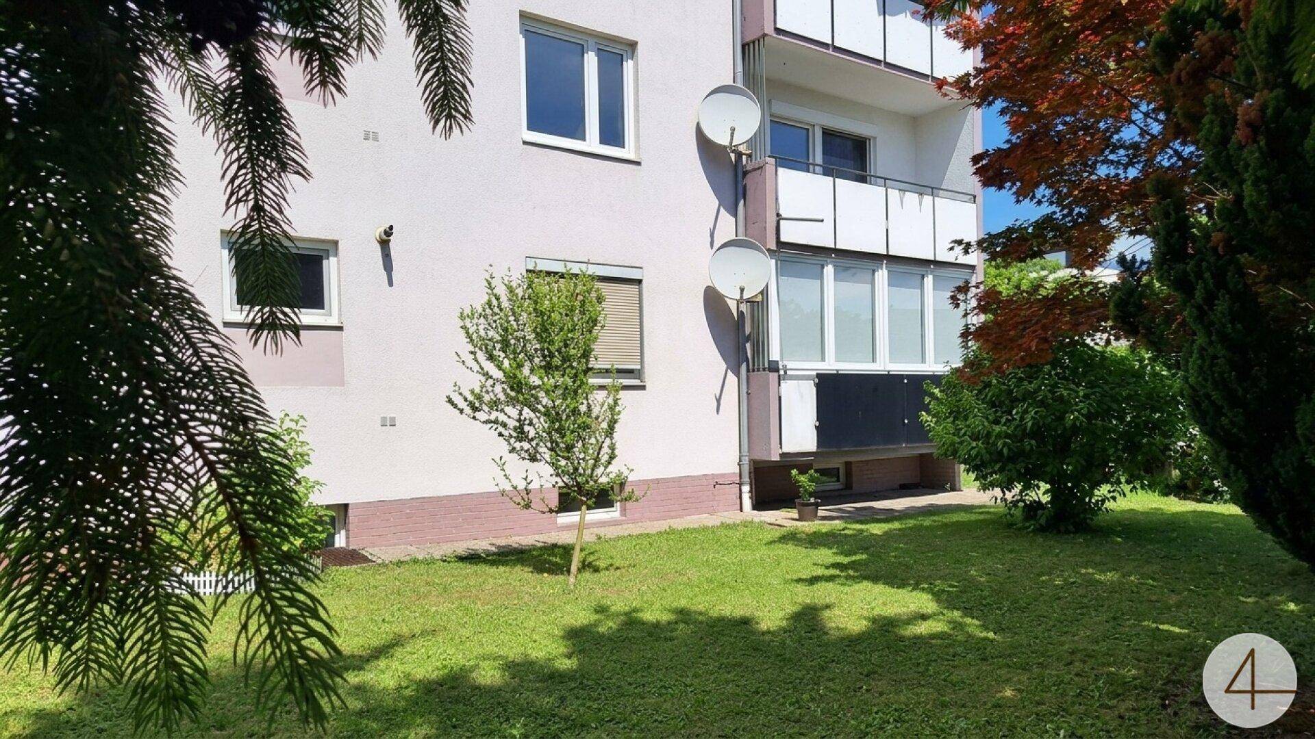 Außenansicht eines Mehrfamilienhauses mit Balkonen und gepflegter Grünfläche im Vordergrund.