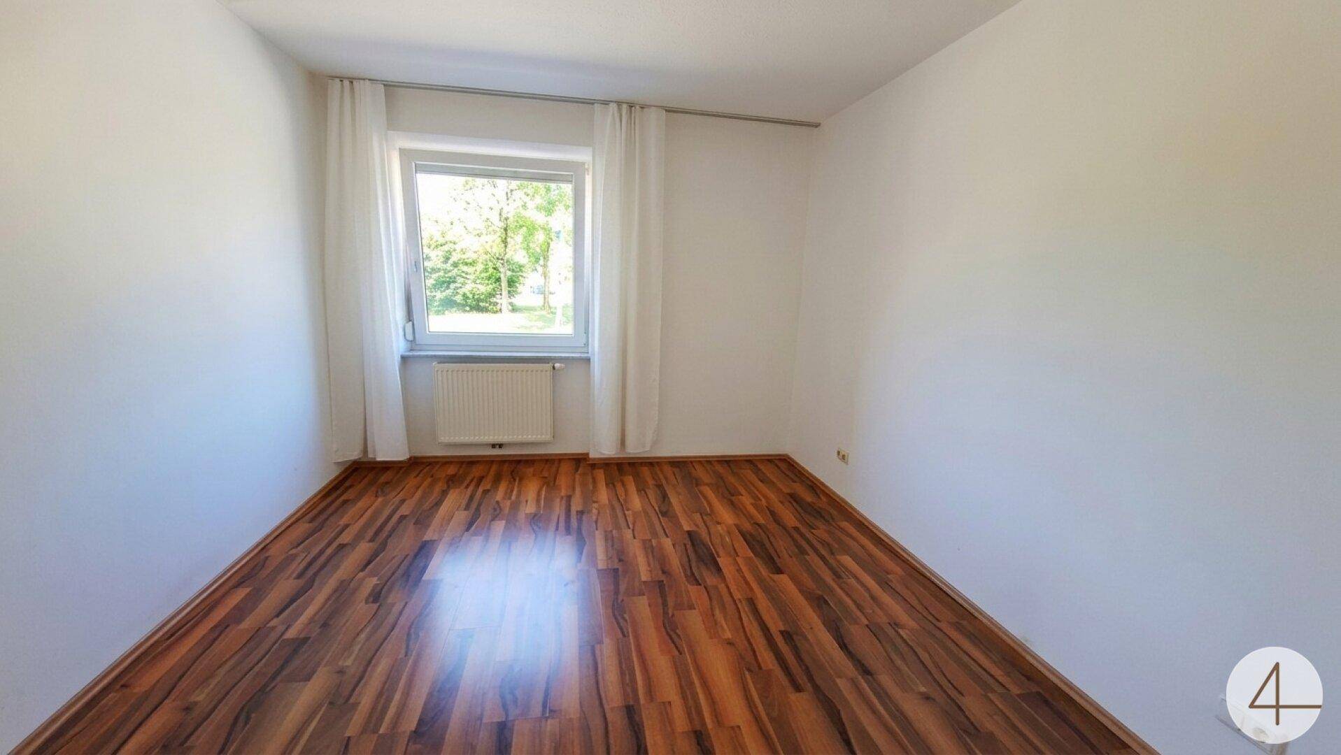 Helles Schlafzimmer mit Holzboden und einem Fenster mit Blick ins Grüne.