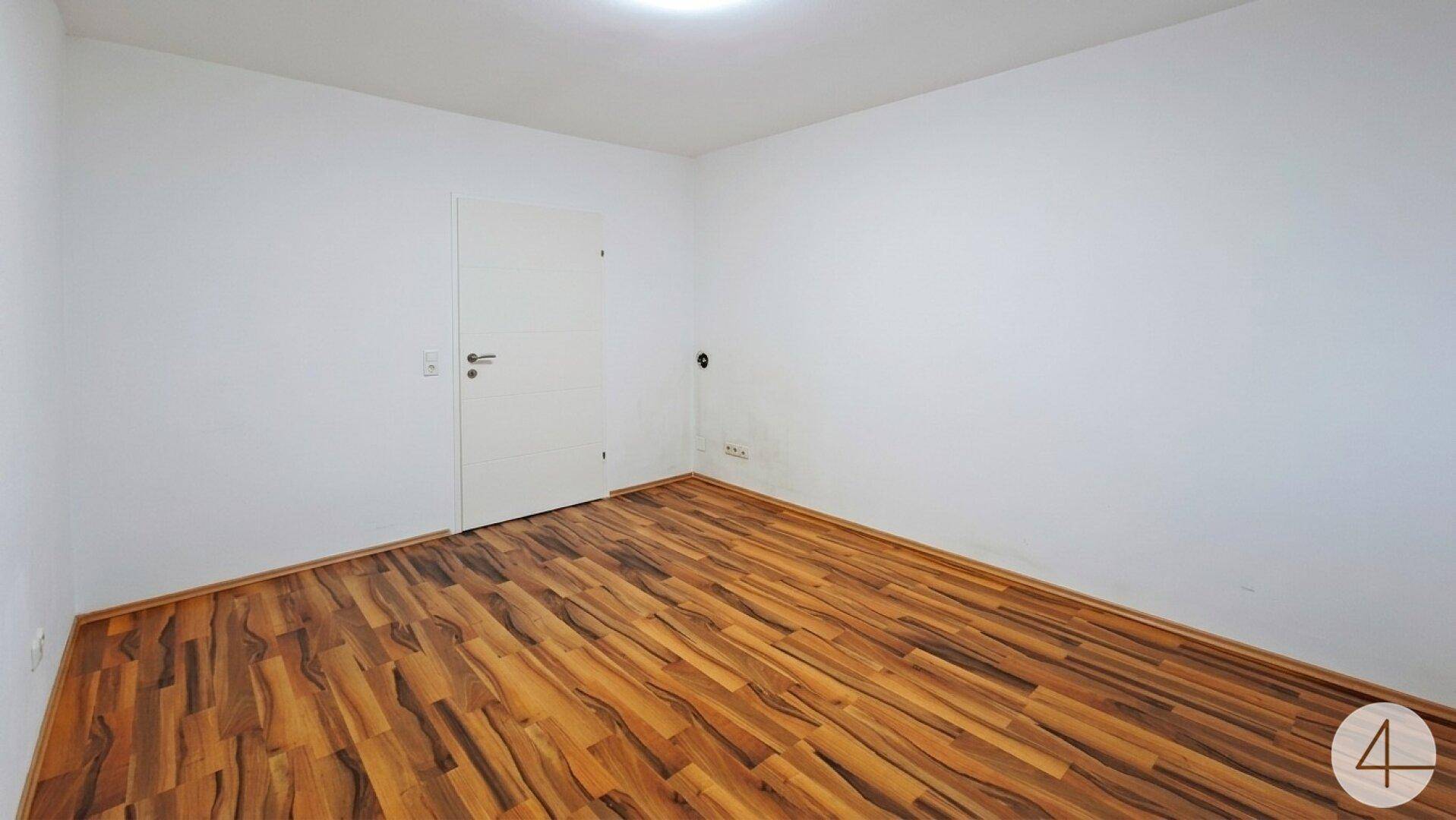 Leerer Raum mit Holzboden und weißer Tür, ideal als Schlaf- oder Arbeitszimmer.