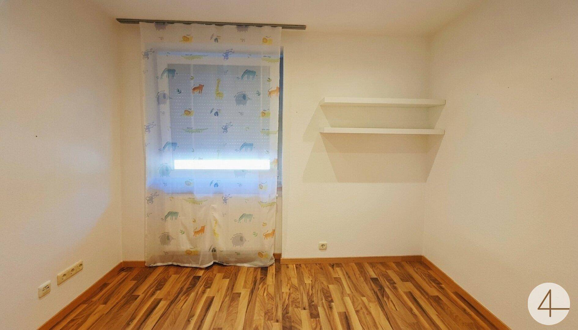 Kinderzimmer mit Holzboden, Fenster und zwei schwebenden Wandregalen.