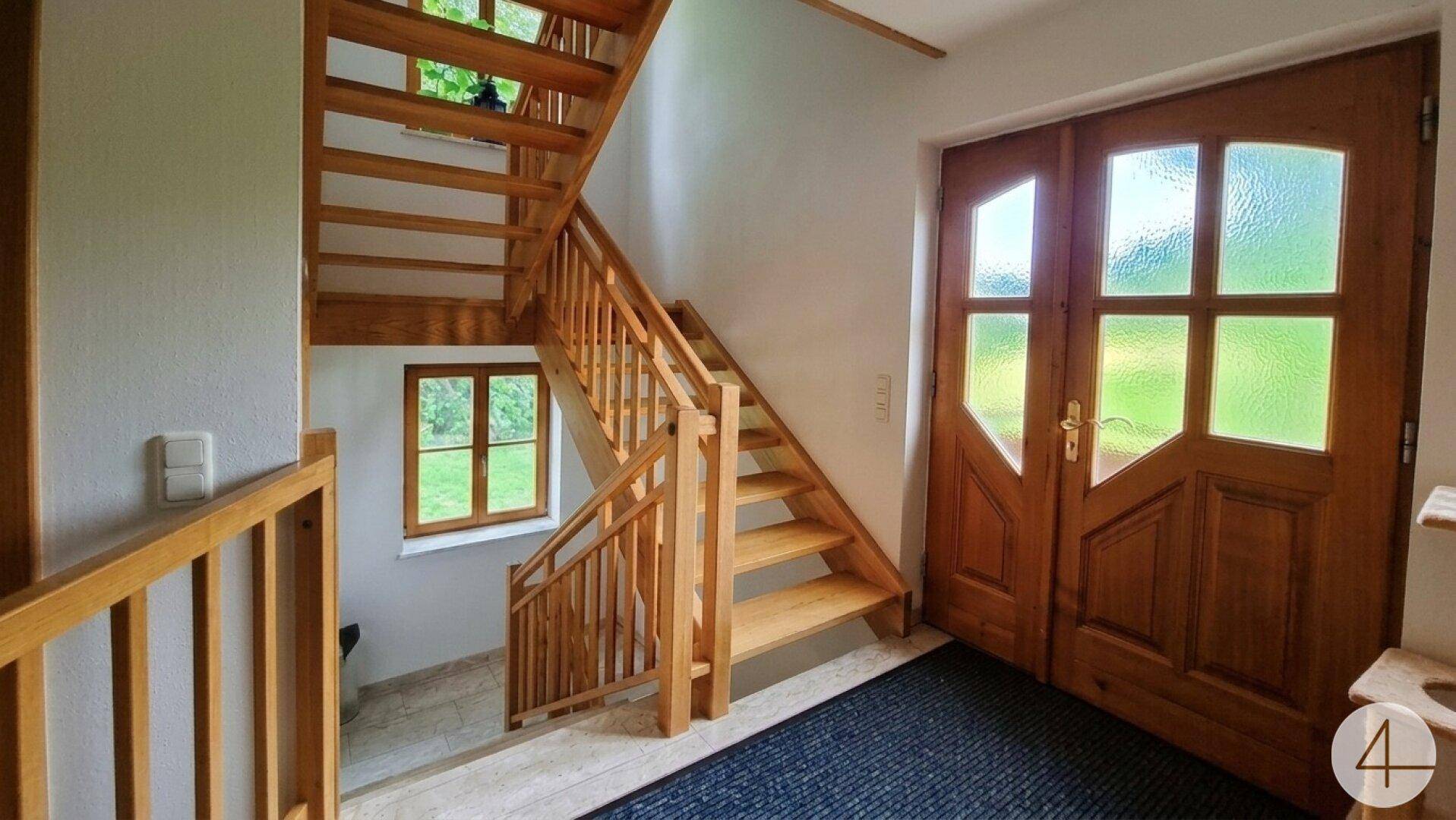 Heller Eingangsbereich mit offener Holztreppe, die zu den oberen Etagen führt.