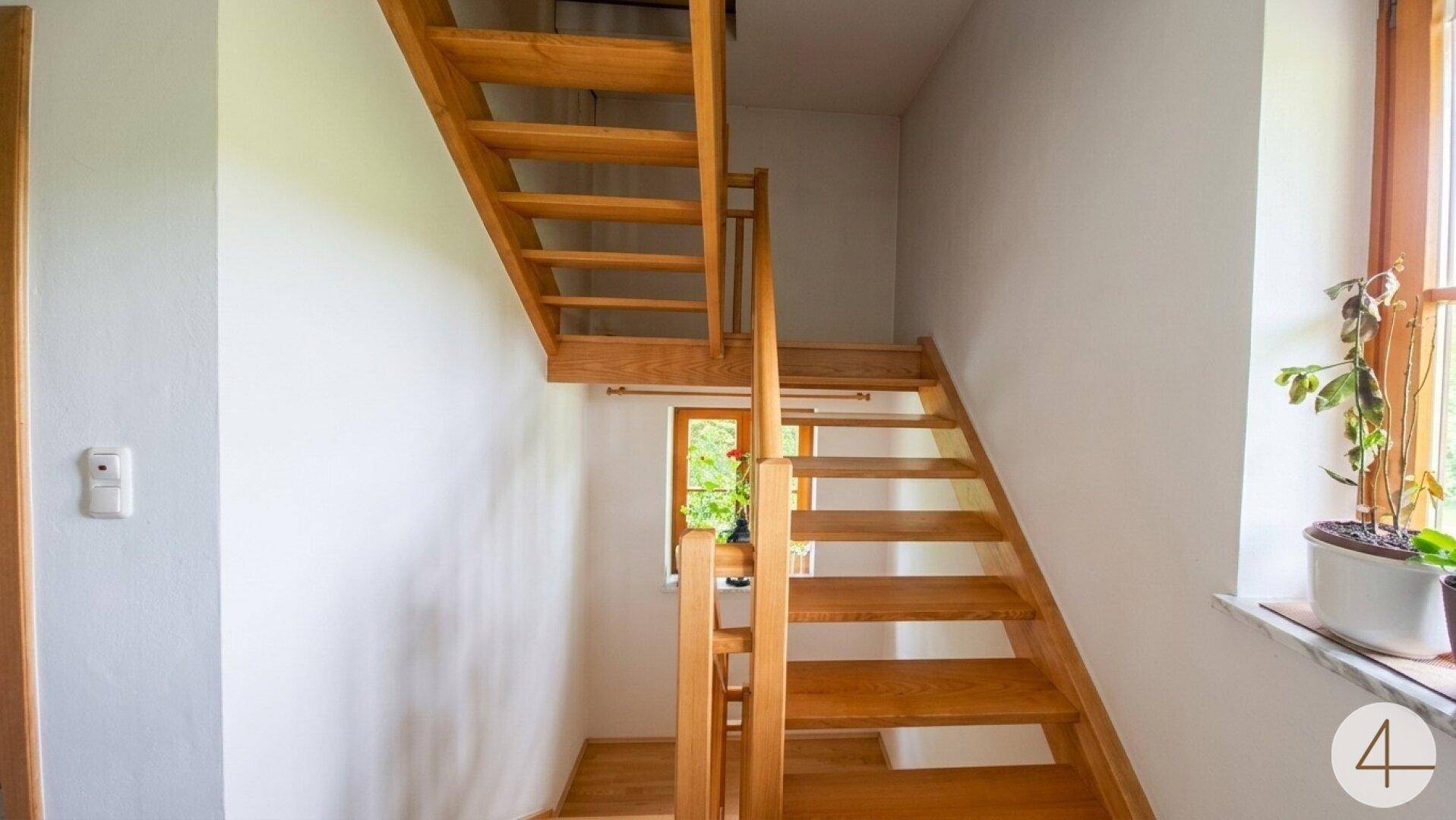 Helle Holztreppe in einem Flur mit weißen Wänden und einem Fenster.