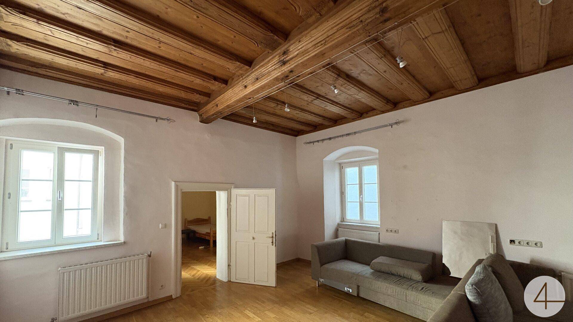 Helles Wohnzimmer mit beeindruckender Holzbalkendecke, weißen Wänden und einem bequemen Sofa.