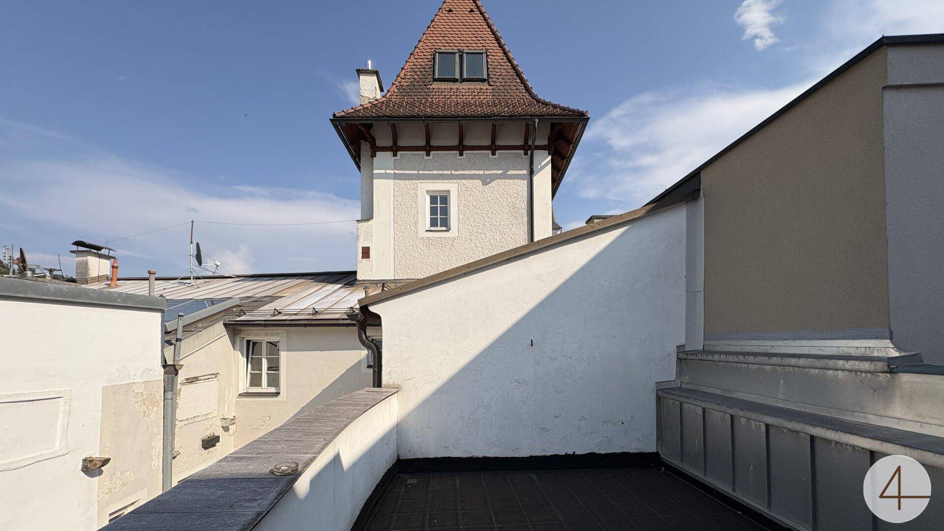 Dachterrasse mit Blick auf einen historischen Turm und die umliegenden Dächer der Stadt.