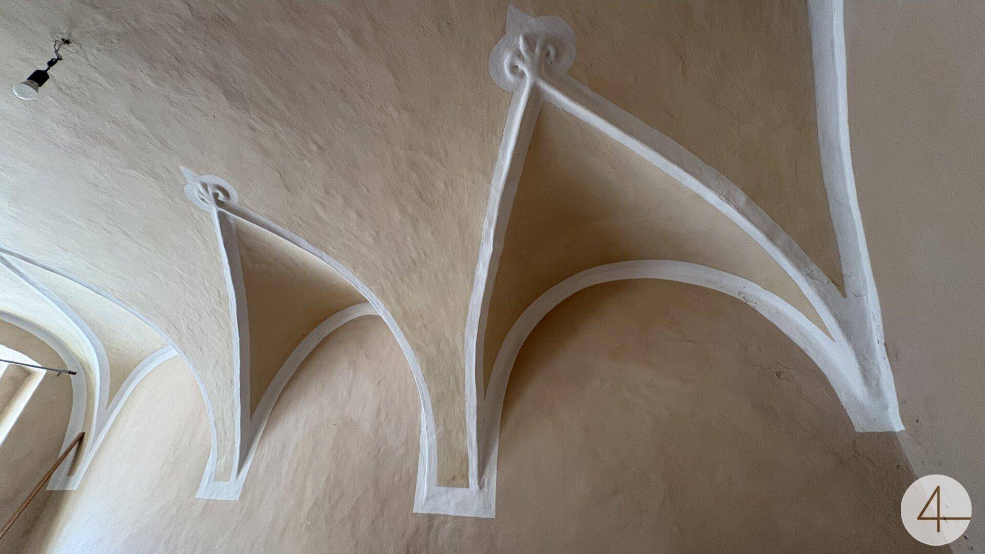 Historische Gewölbedecke mit eleganten weißen Rippen auf beigem Hintergrund, die architektonische Details zeigt.