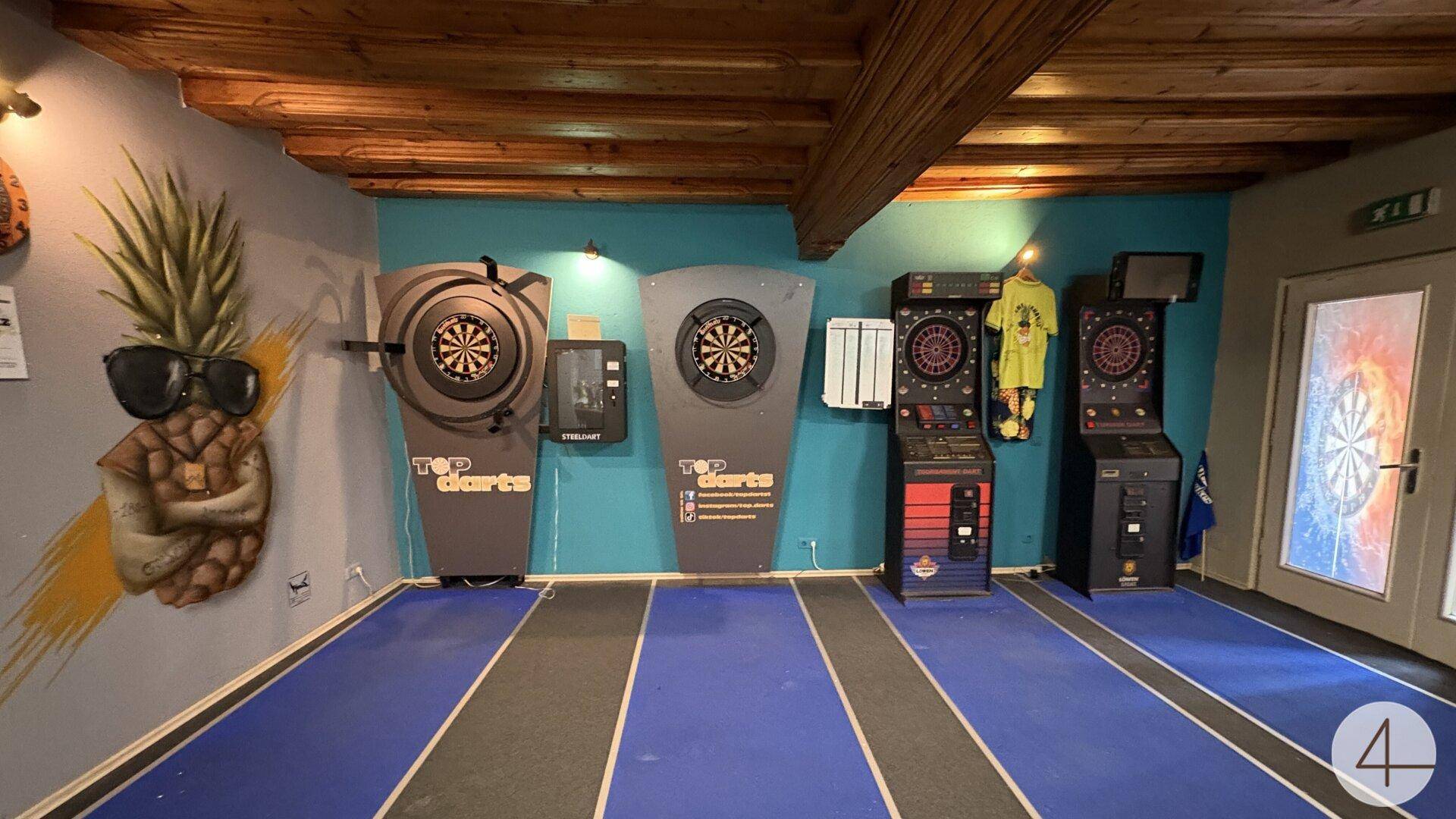 Lebhaftes Spielzimmer mit mehreren Dartautomaten, farbigen Wänden und sichtbaren Holzdeckenbalken.
