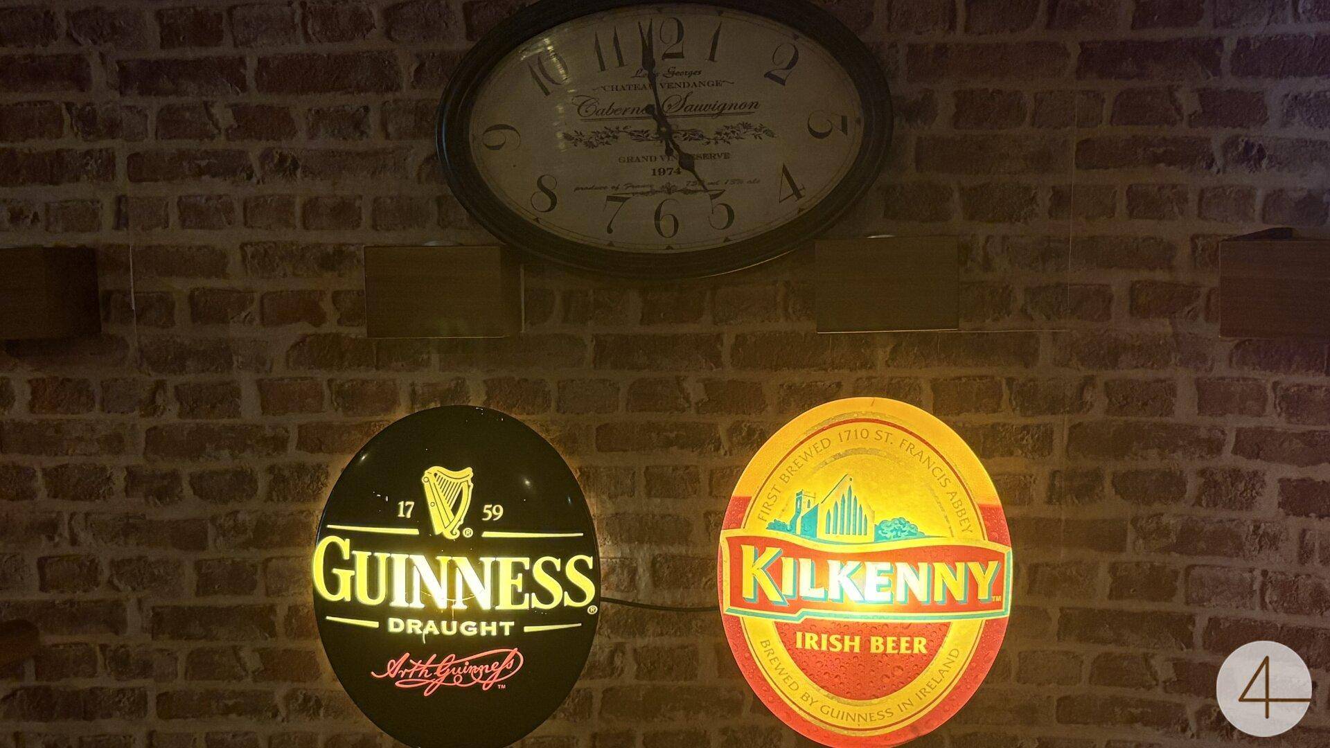 Ziegelwand mit großer Uhr und beleuchteten Guinness- und Kilkenny-Bierschildern als Dekoration.