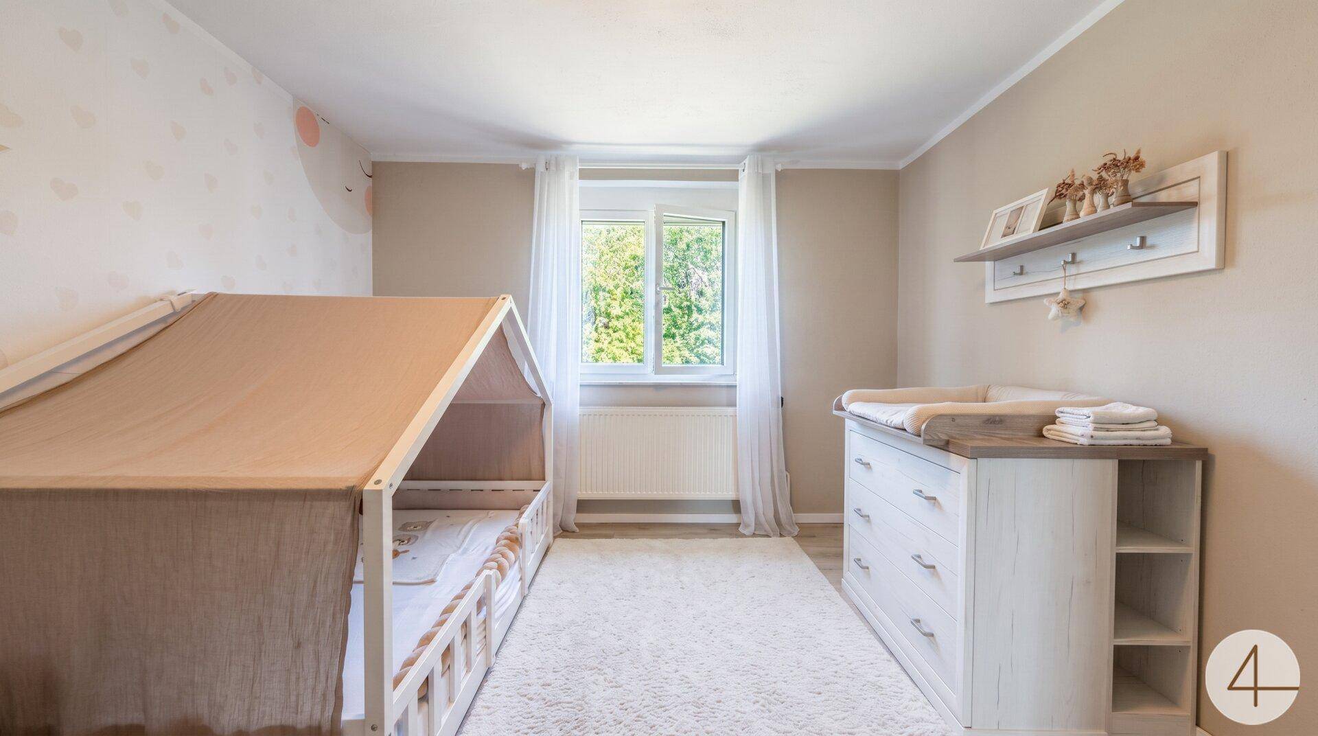 Helles Kinderzimmer mit Wickelkommode, Hausbett und Fenster für natürliches Licht.