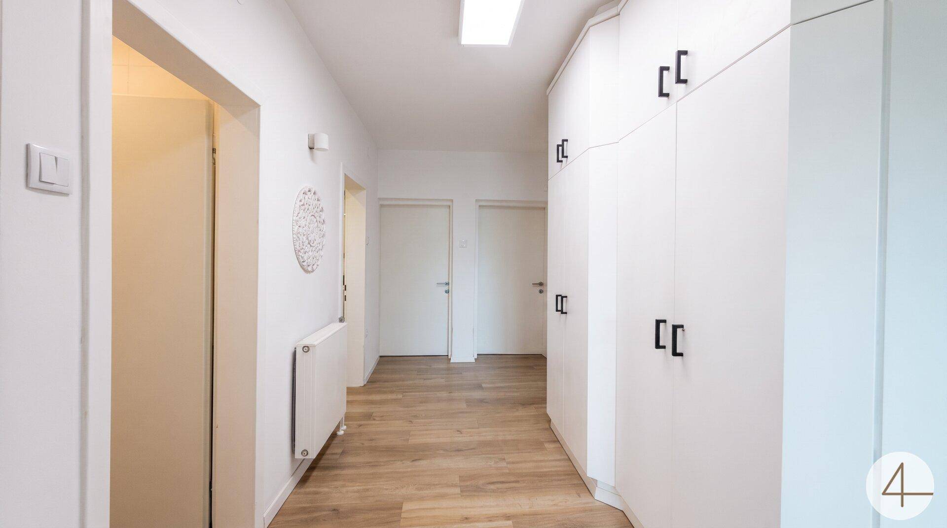 Geräumiger Flur mit hellem Laminatboden, weißen Wänden und Heizkörper.