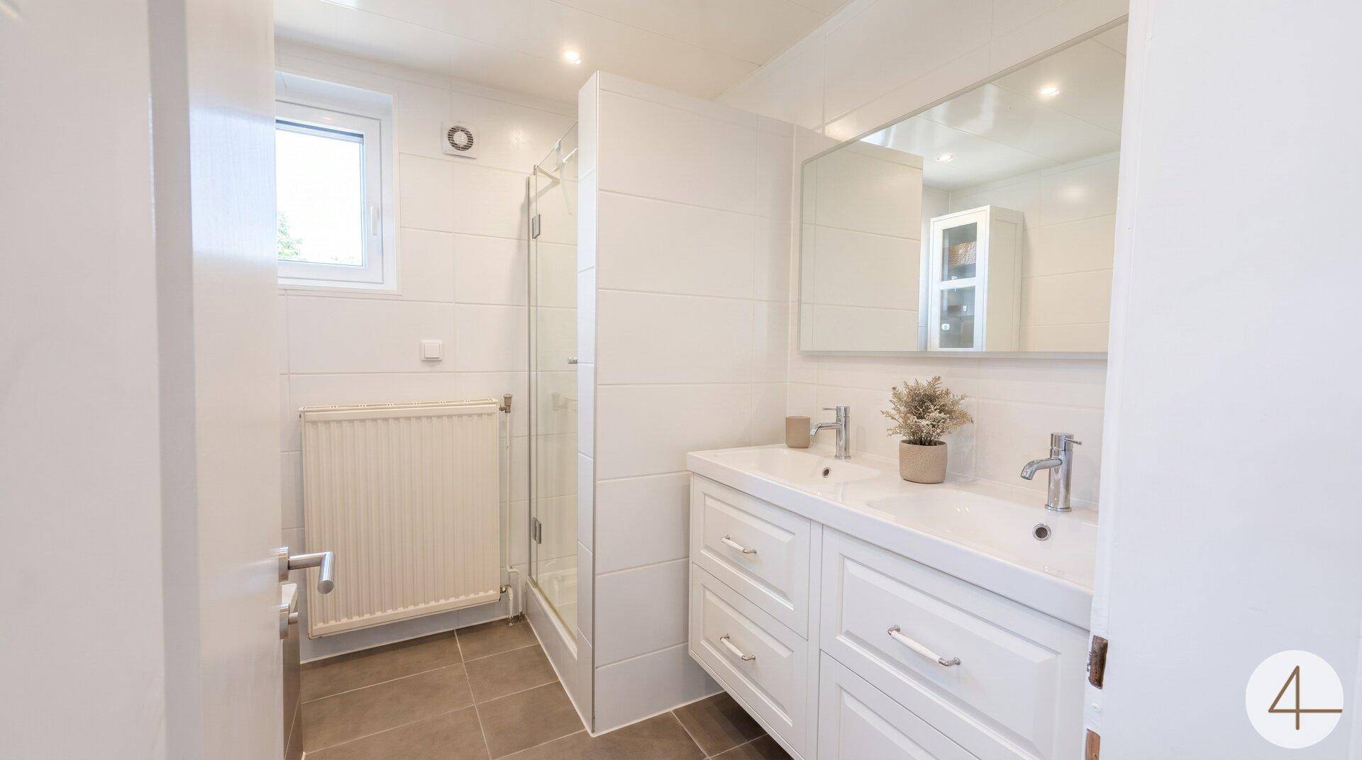Modernes Badezimmer mit Doppelwaschbecken, Duschkabine und Fenster für Tageslicht.