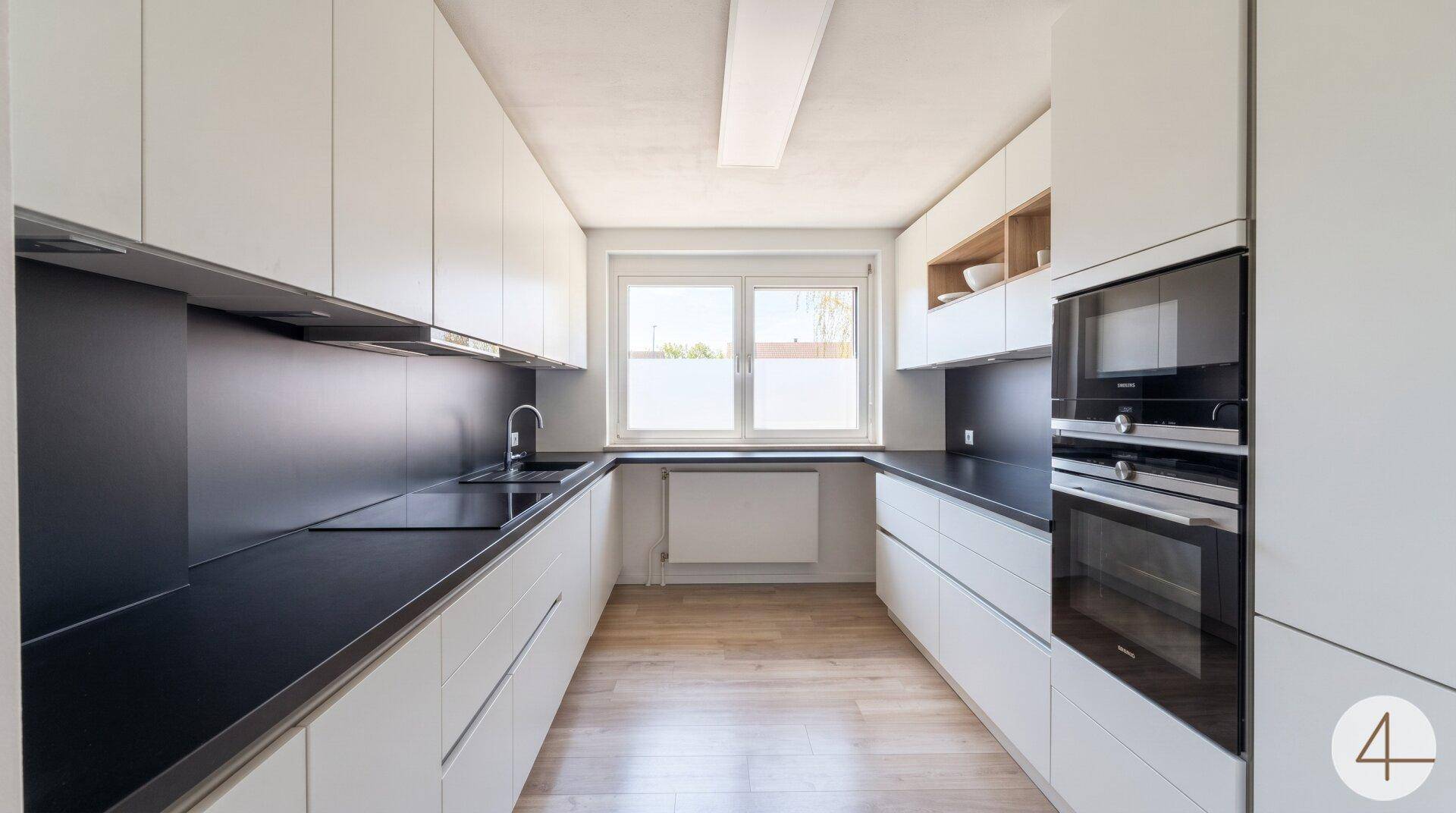 Moderne Küche mit weißen Schränken, schwarzen Arbeitsplatten und integrierten Geräten.