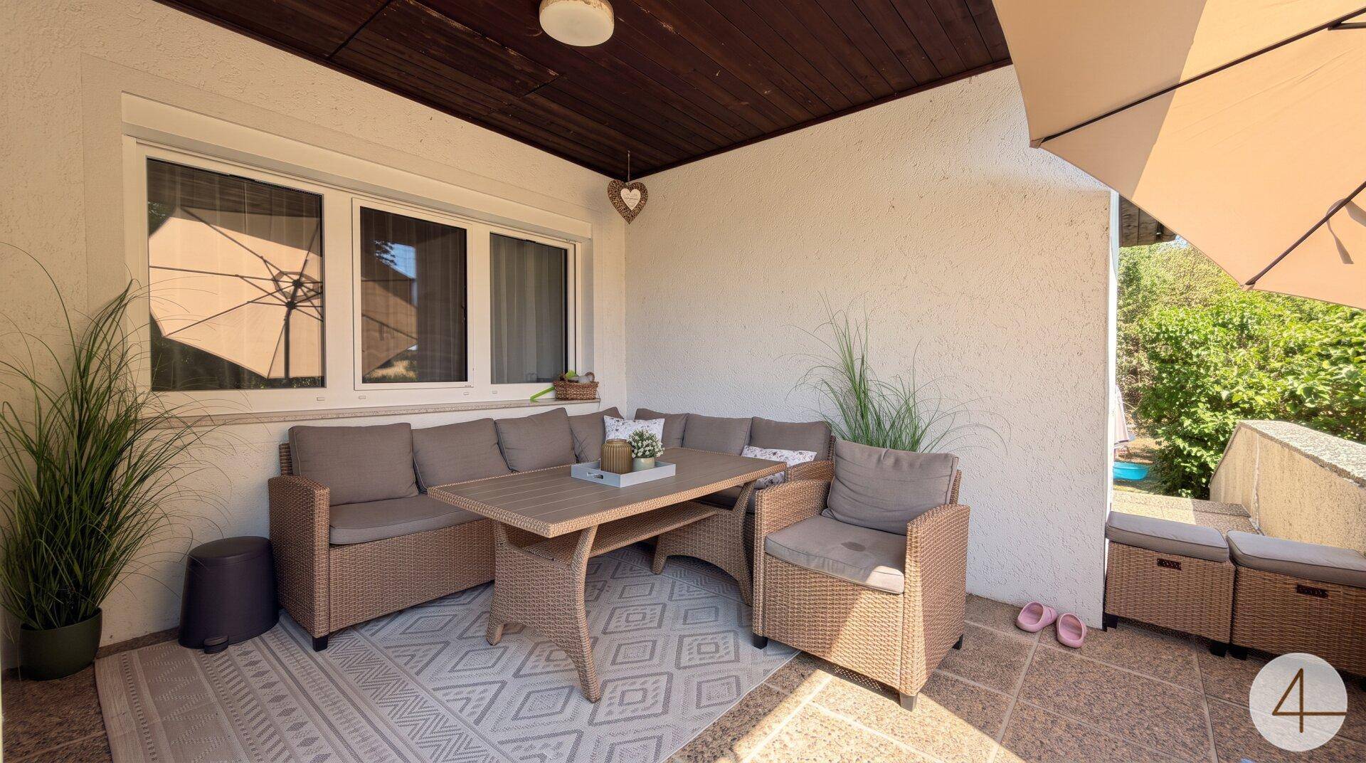 Gemütliche überdachte Terrasse mit Rattanmöbeln und einem Teppich für entspannte Stunden.