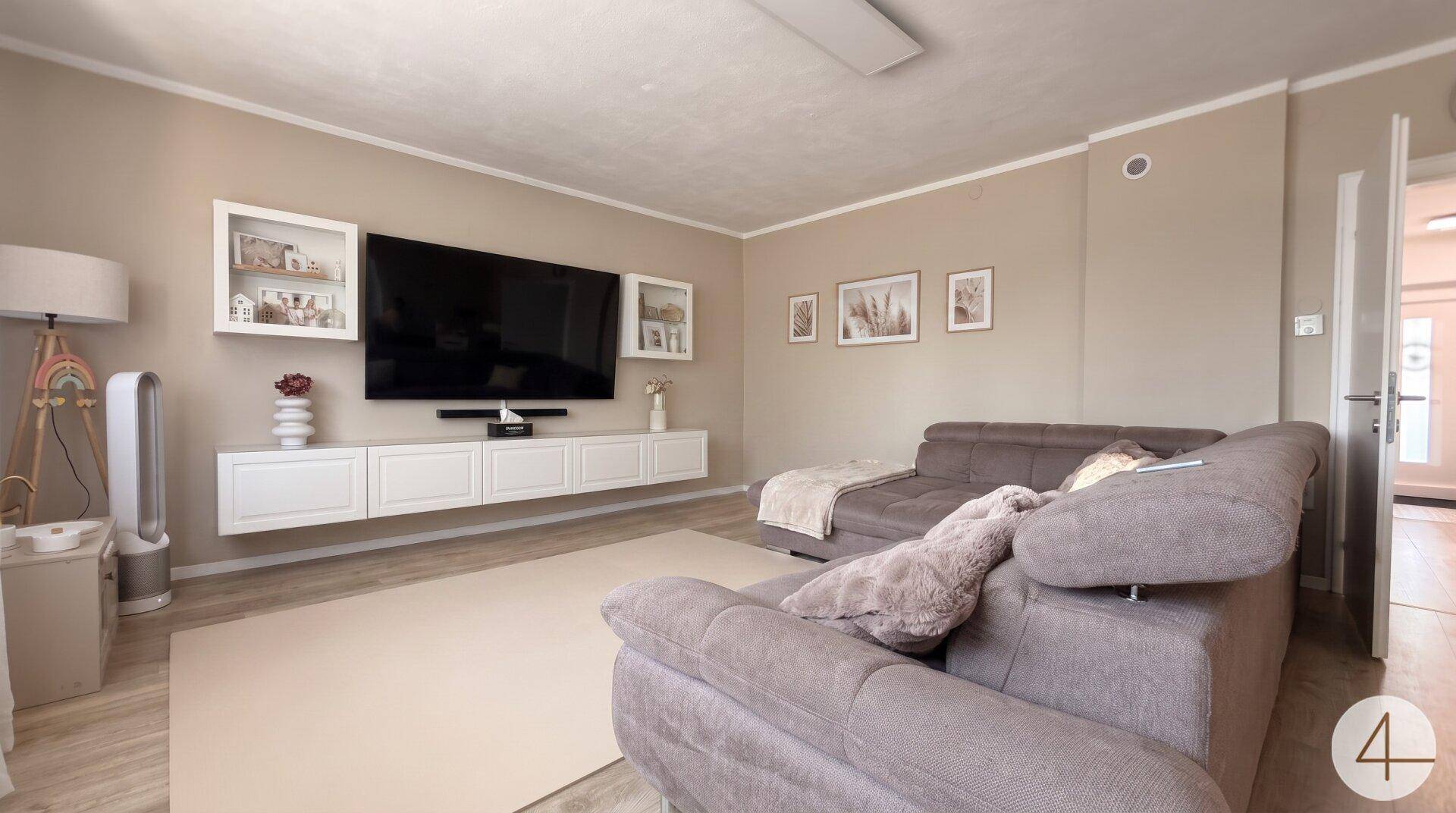 Geräumiges Wohnzimmer mit großem Sofa, Wandfernseher und moderner Dekoration.