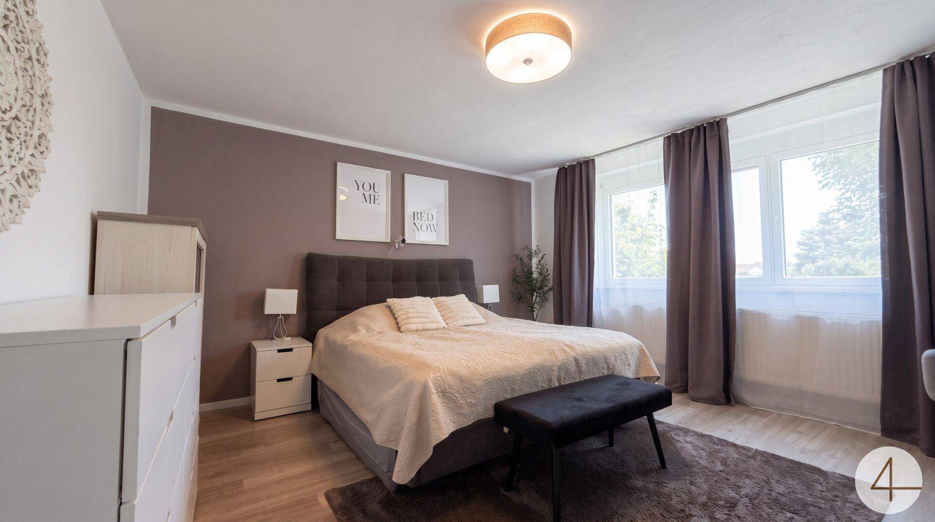 Gemütliches Schlafzimmer mit Doppelbett, Nachttischen und großen Fenstern.