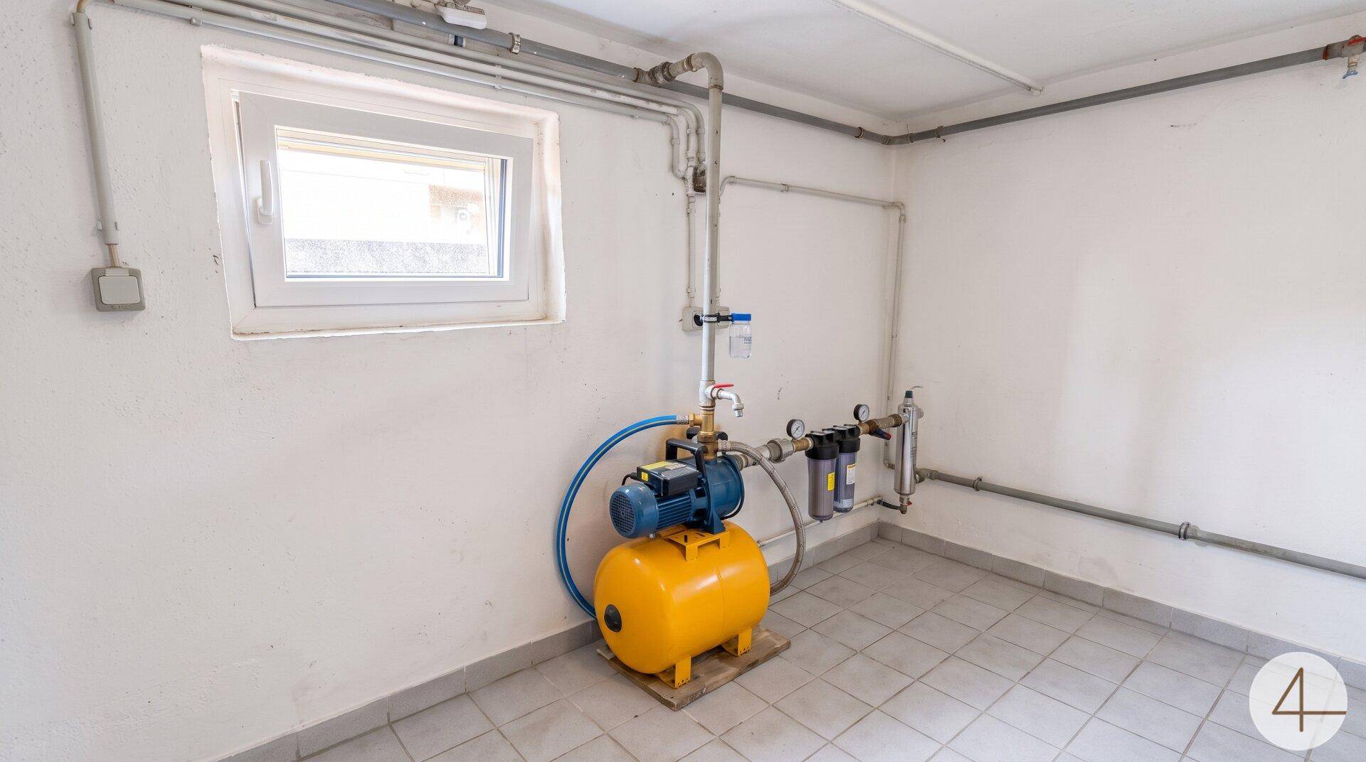 Technikraum im Keller mit Wasserpumpe, Filtersystem und einem Fenster.