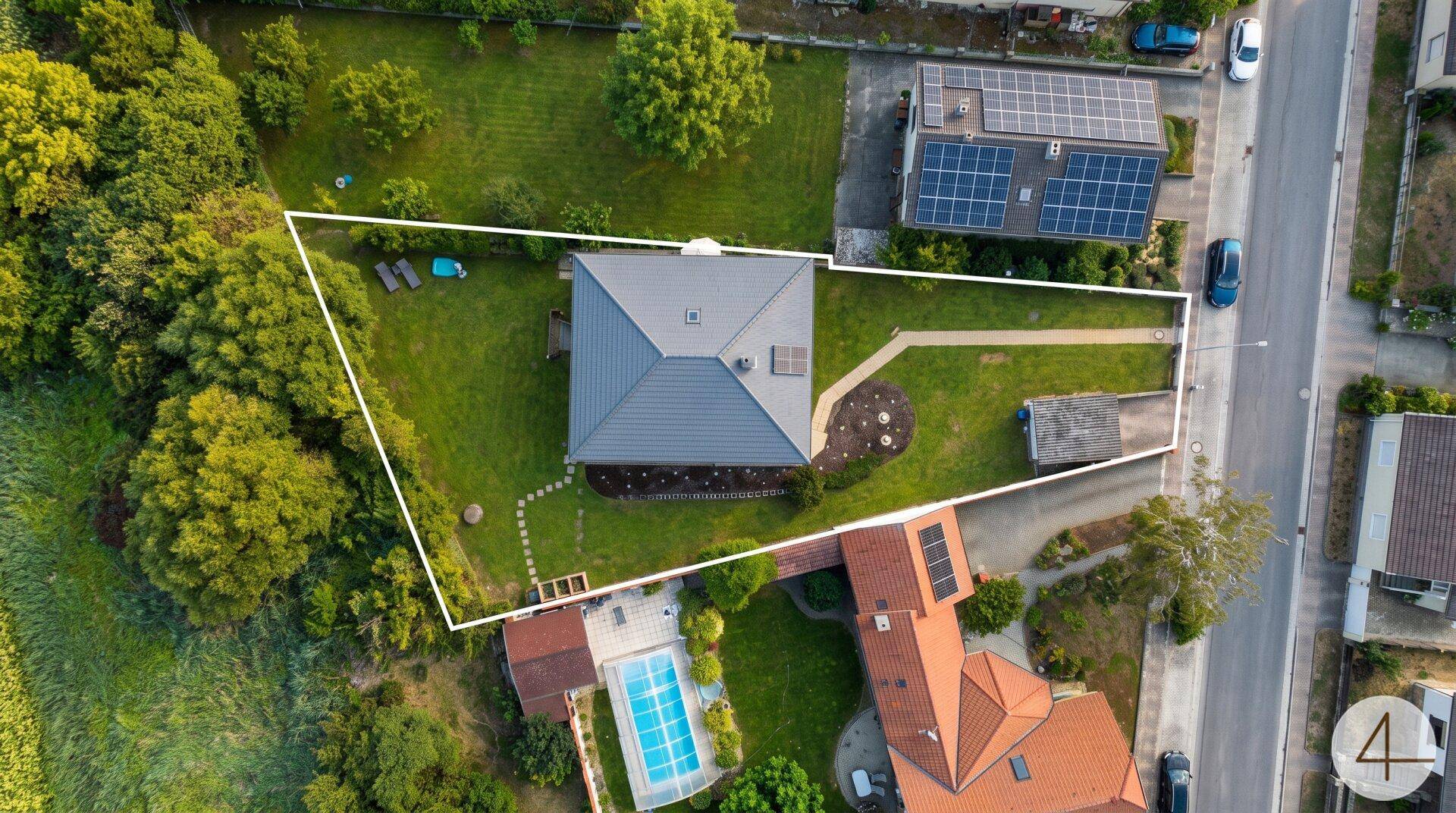 Vogelperspektive des Grundstücks mit Haus, Garten und angrenzender Straße, umrandet von einer weißen Linie.