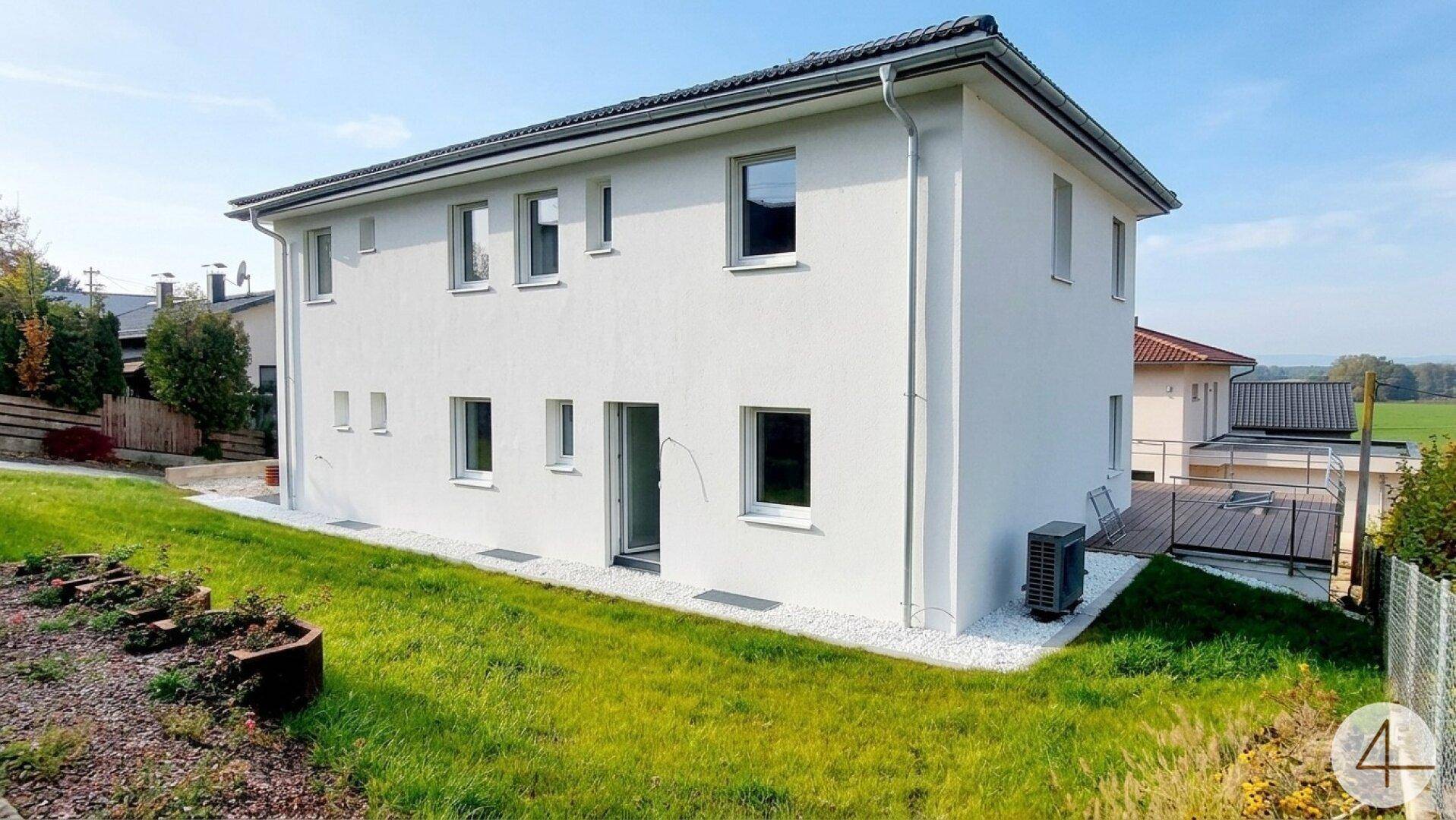 Rückseite des Neubaus mit gepflegtem Rasen, kleiner Terrasse und moderner Klimaanlage.