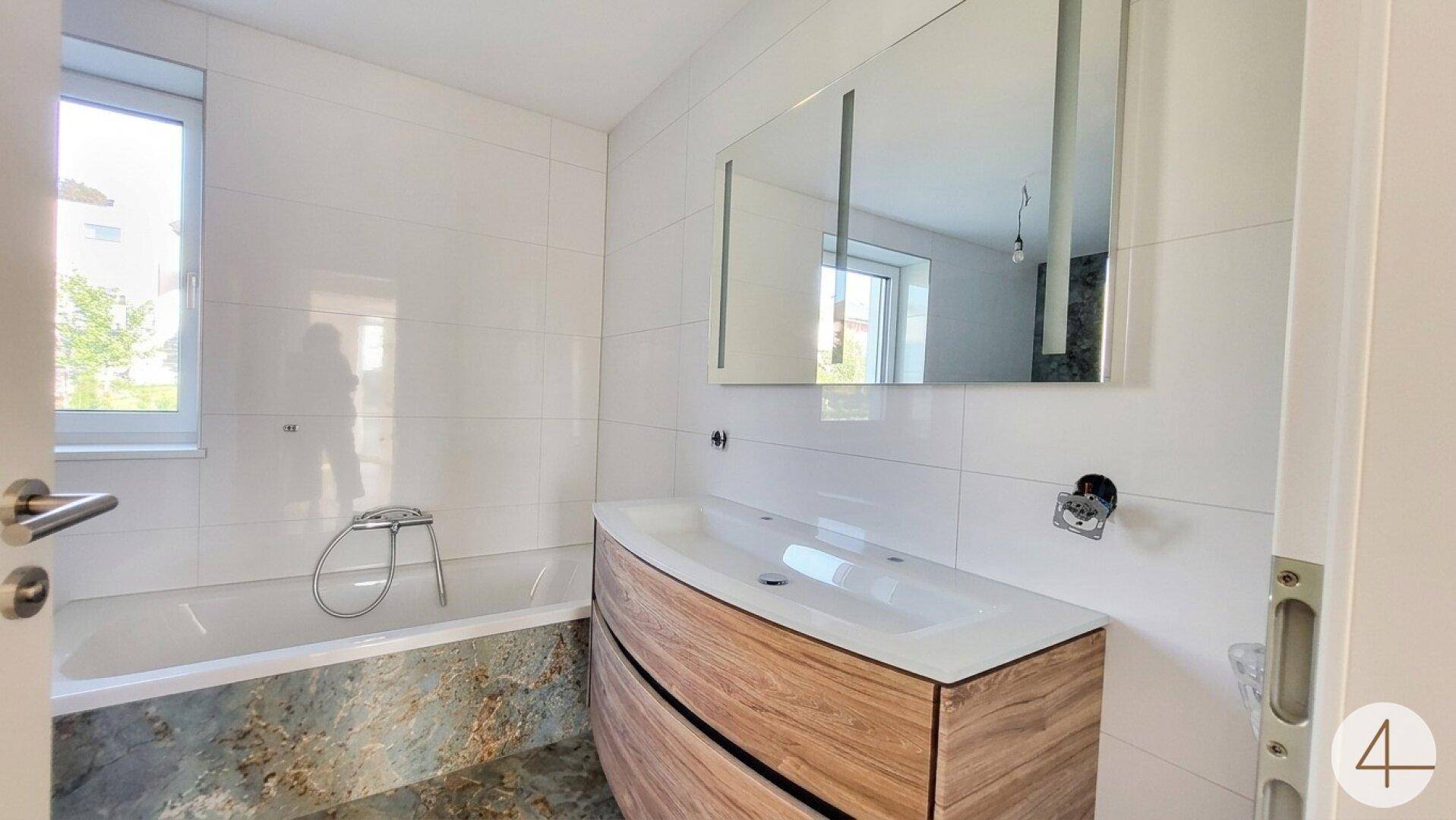 Modernes Badezimmer mit Badewanne, Holzwaschtisch und Spiegelschrank.