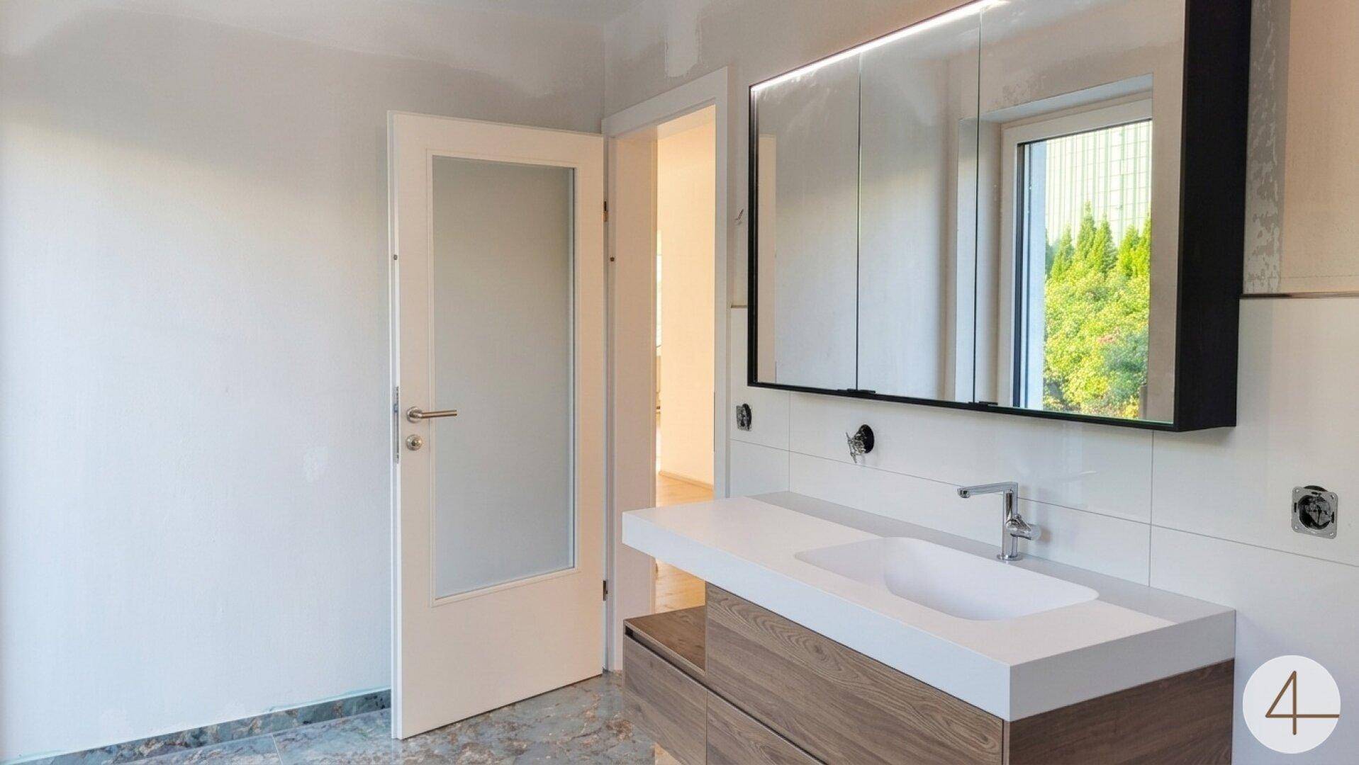 Helles Badezimmer mit modernem Waschtisch, Spiegelschrank und Fenster.