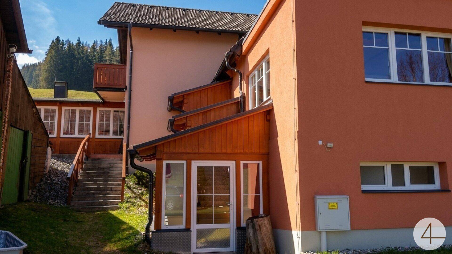 Seitenansicht eines Gebäudes mit orangefarbener Fassade und Holzverkleidung, umgeben von grüner Wiese.