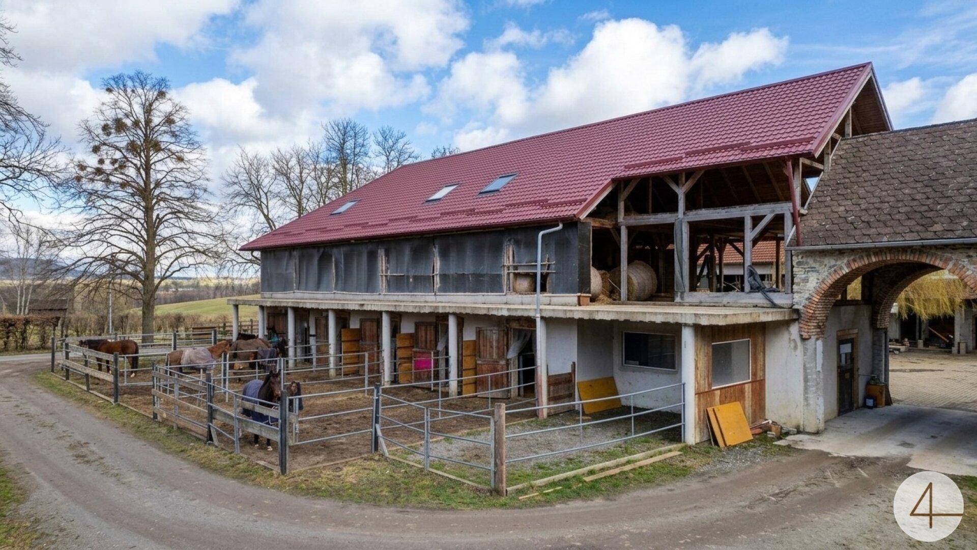 Großes Stallgebäude mit rotem Dach, Pferdekoppeln und angrenzendem Torbogen.