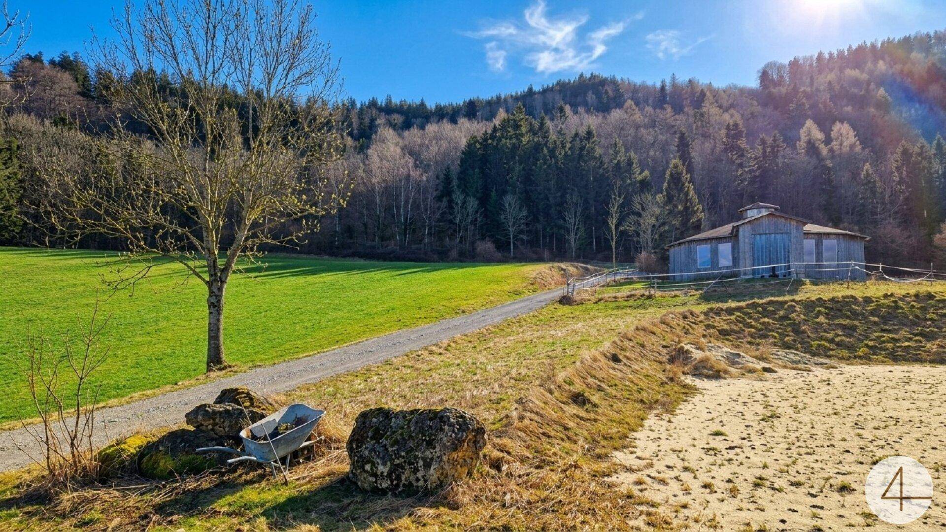 Weitläufige grüne Landschaft mit einem Gebäude im Hintergrund und bewaldeten Hügeln unter blauem Himmel.