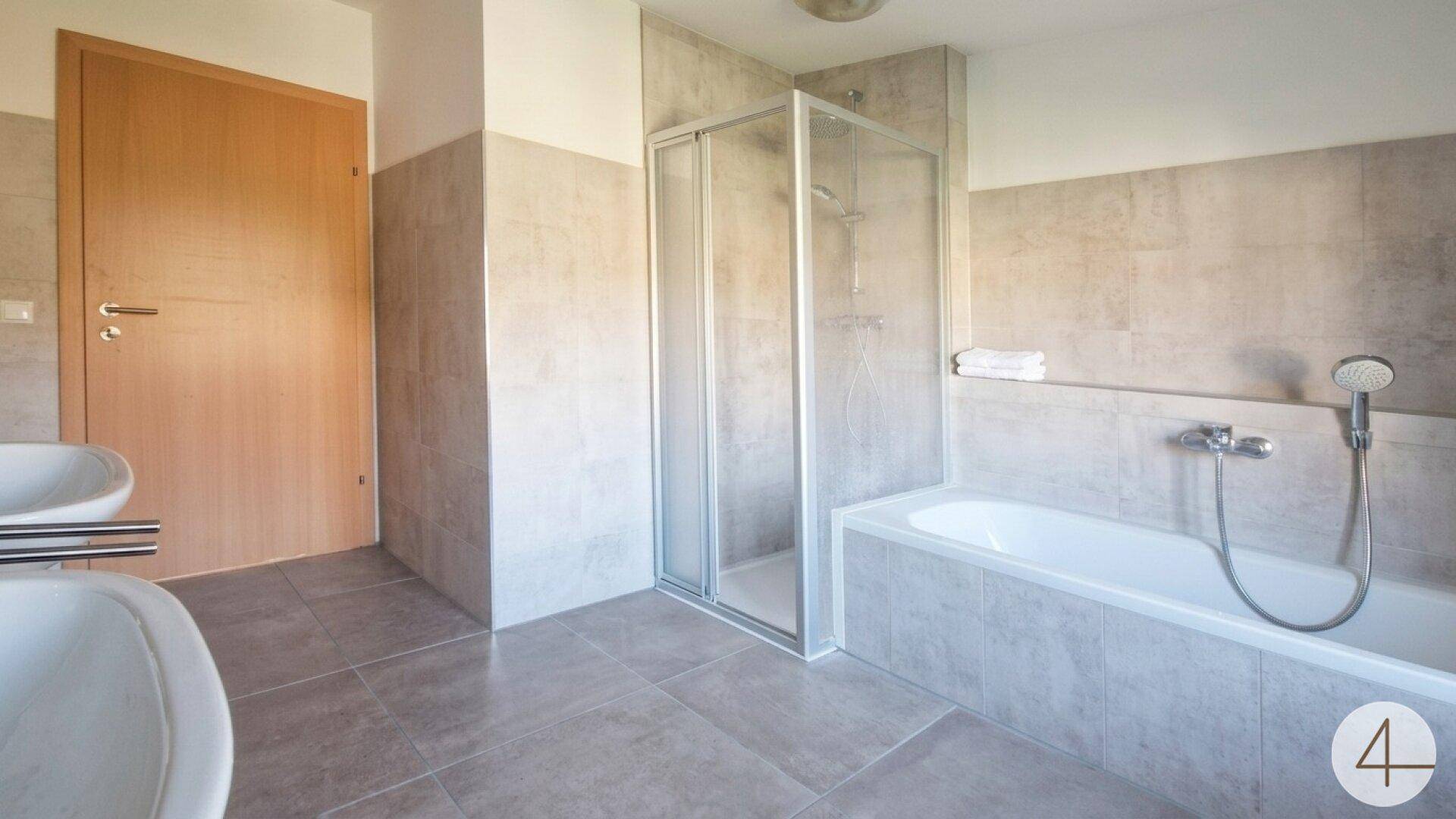 Modernes Badezimmer mit grauen Fliesen, Badewanne und Duschkabine, ausgestattet mit einem einzelnen Waschbecken.