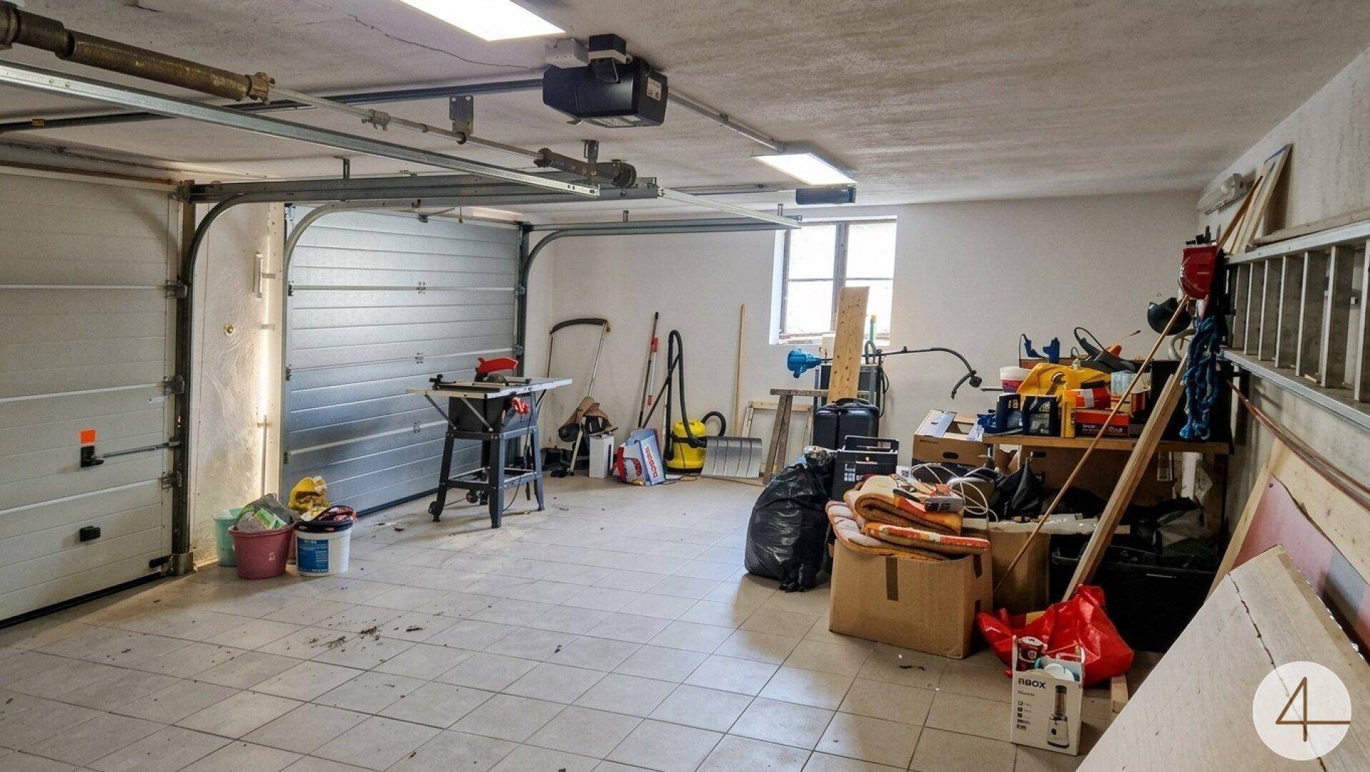 Geräumige Garage mit automatischem Tor, gefliestem Boden und viel Stauraum für Werkzeuge und Geräte.