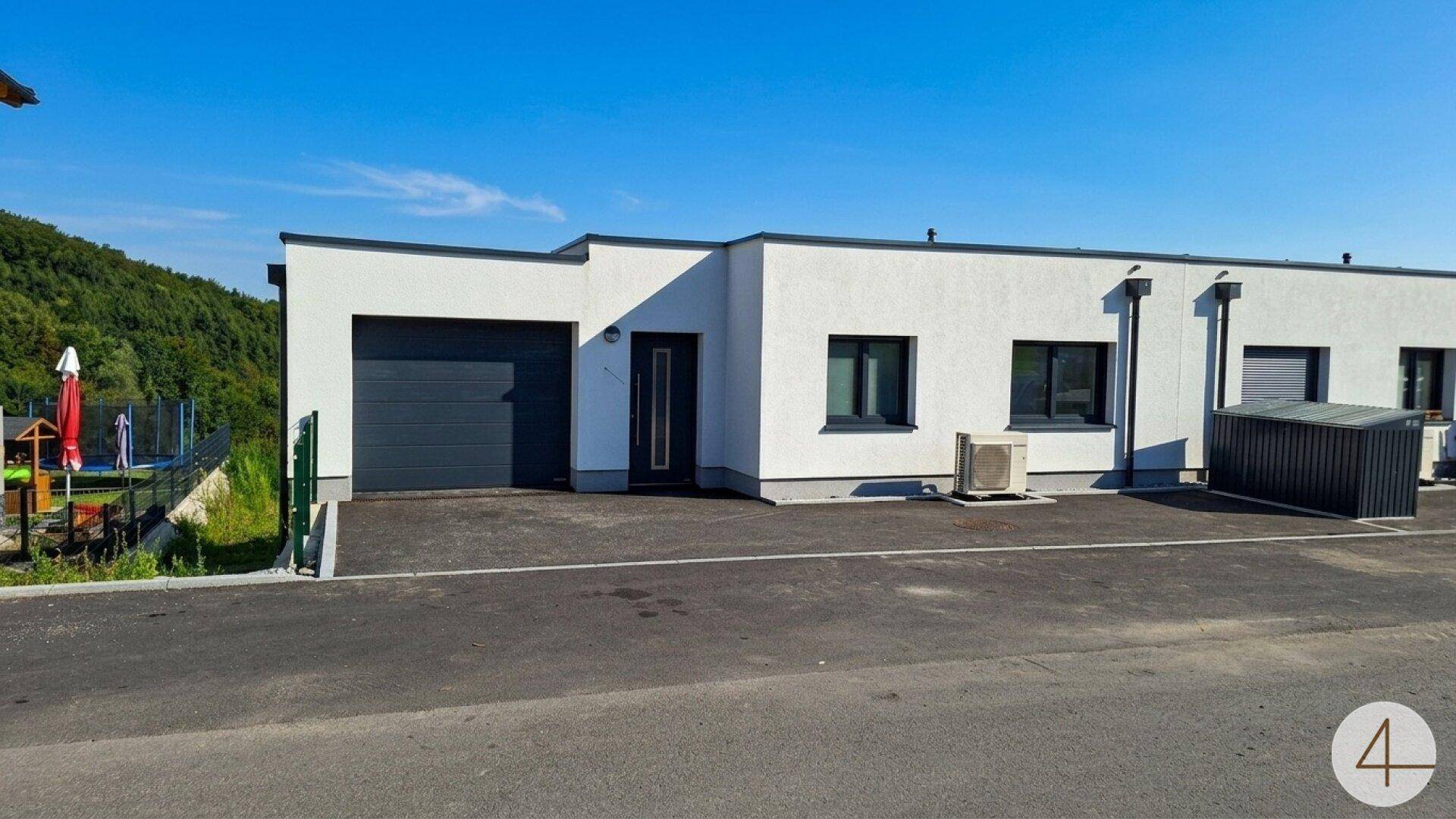 Vorderansicht eines modernen Reihenhauses mit Garage, Einfahrt und schlichter weißer Fassade unter blauem Himmel.