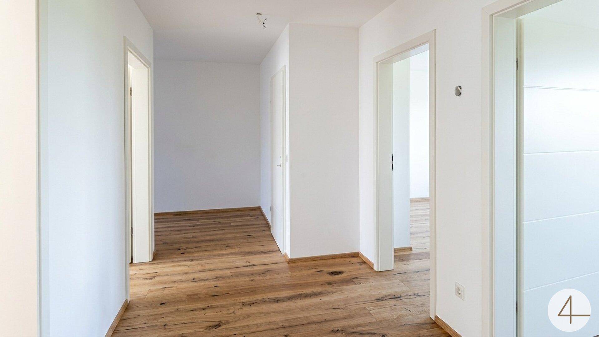 Geräumiger Flur mit hellem Holzboden und weißen Wänden, der zu verschiedenen Zimmern im Haus führt.