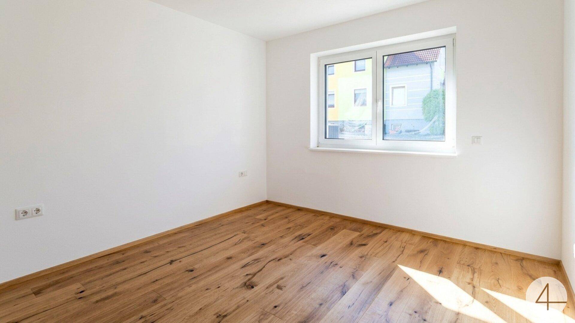 Helles Schlafzimmer mit Holzboden und einem großen Fenster, das viel Tageslicht in den Raum lässt.