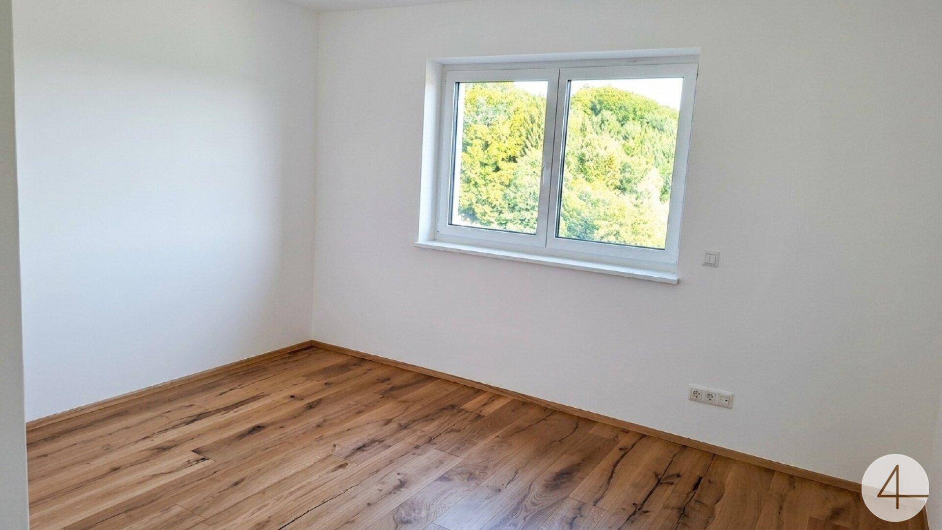 Ruhiges Schlafzimmer mit Holzboden und Fenster, das einen angenehmen Blick ins Grüne ermöglicht.