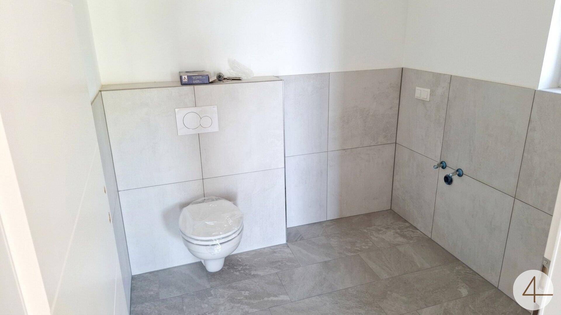 Modernes Gäste-WC mit hellgrauen Fliesen und wandhängendem WC, noch in der Fertigstellungsphase.