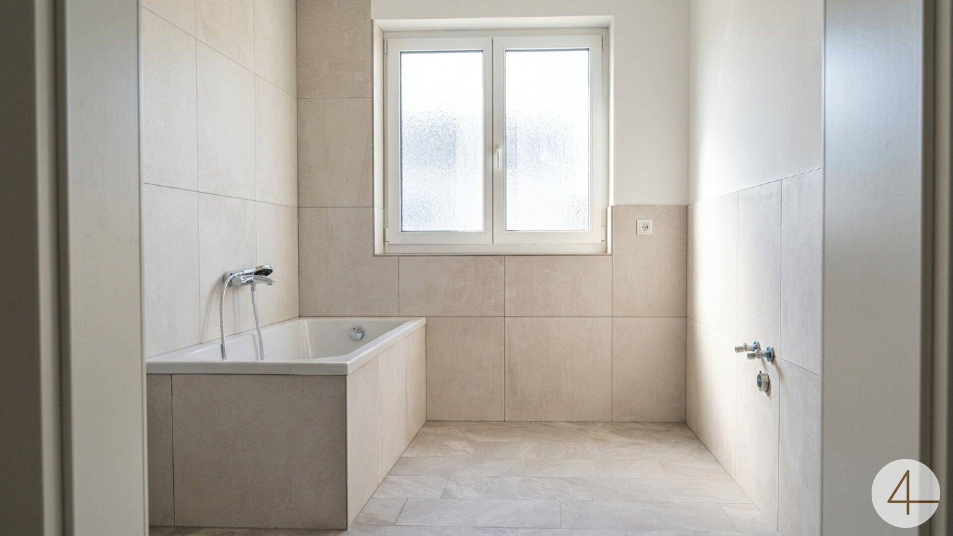 Helles Badezimmer mit Badewanne, beigefarbenen Fliesen und Fenster, bereit für die Endmontage der Armaturen.
