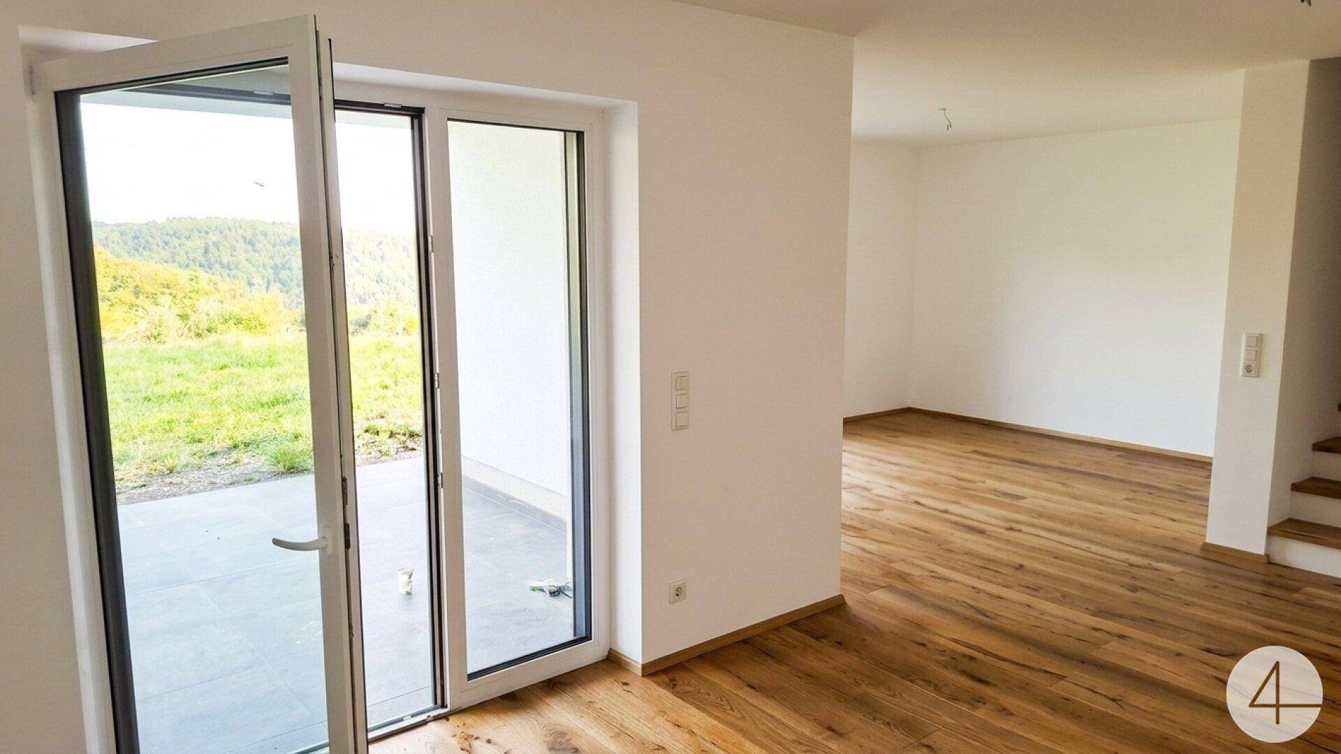 Geräumiger Wohnbereich mit Holzboden und offener Terrassentür, die viel Licht und frische Luft hereinlässt.